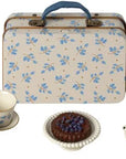 A floral Maileg Furniture suitcase with blue handle sits behind a cute toy tea set—perfect for Maileg mouse or dollhouse—including a white teapot, teacups, and a plate with chocolate cake topped with blueberries.