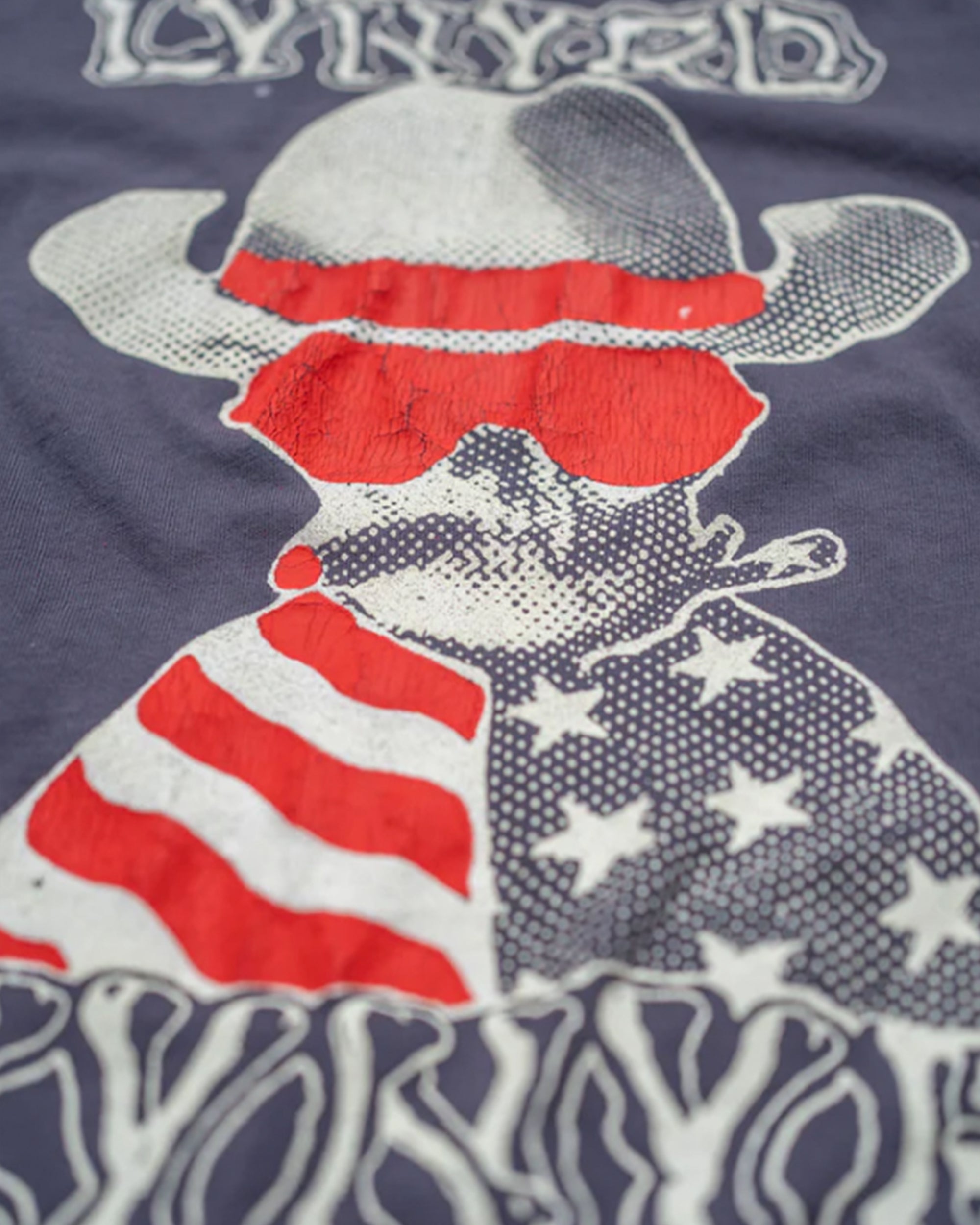 Lynyrd Skynyrd Crew Tee by Made Worn features a dog in a cowboy hat and red sunglasses with an American flag, stylized text on a dark background. This vintage unisex t-shirt is 100% cotton and proudly made in the USA.
