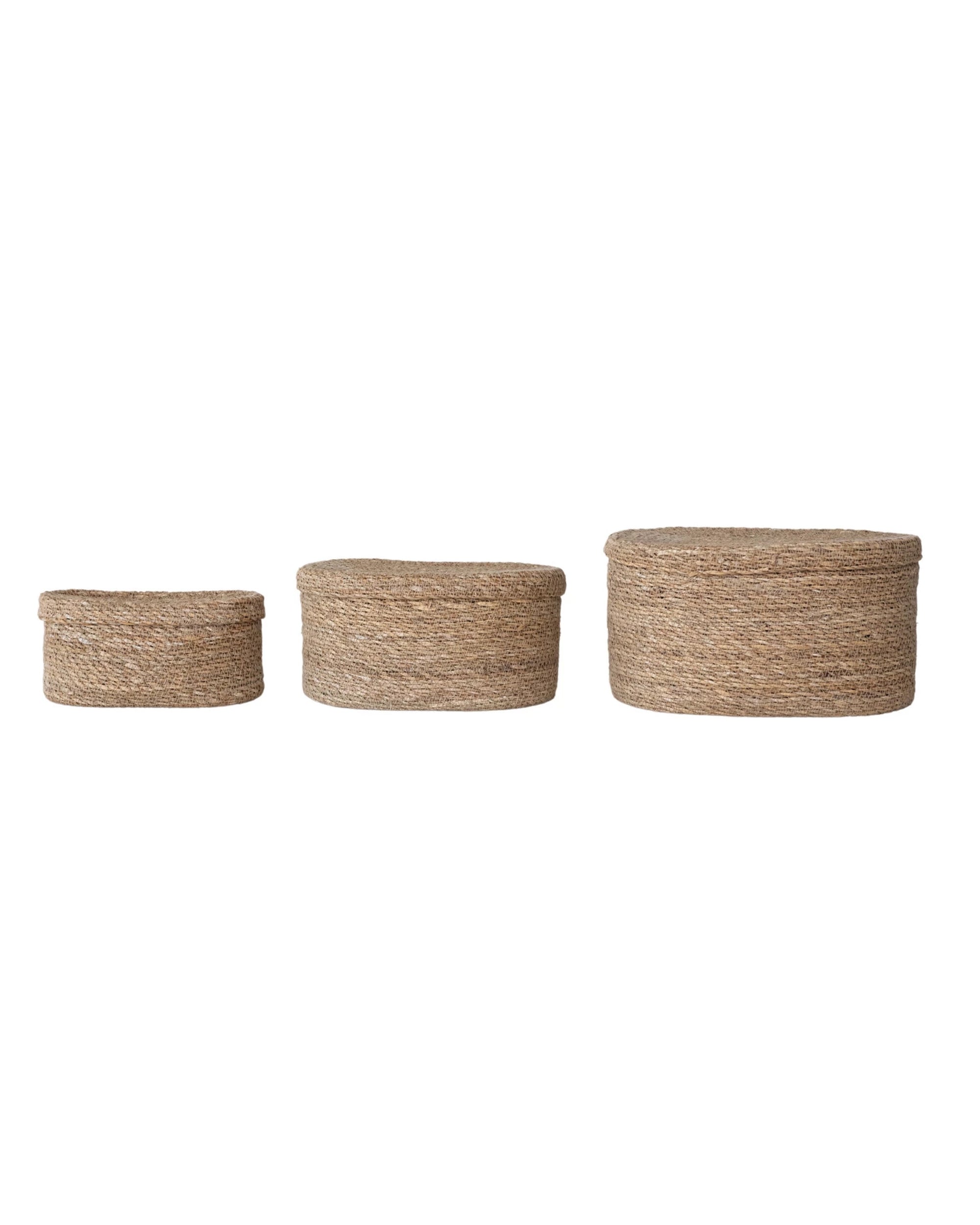 Three Creative Co-op Sea Grass Basket (Long Oval) storage baskets, hand-woven from natural fibers with lids, are lined up in size order from smallest to largest on a white background.