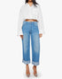 A person wearing Mother’s The Smoothie Crop Cuff jeans and a loose white button-up shirt with rolled-up sleeves, paired with clear pointed-toe heels, stands against a plain white background.