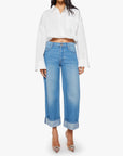 A person wearing Mother’s The Smoothie Crop Cuff jeans and a loose white button-up shirt with rolled-up sleeves, paired with clear pointed-toe heels, stands against a plain white background.