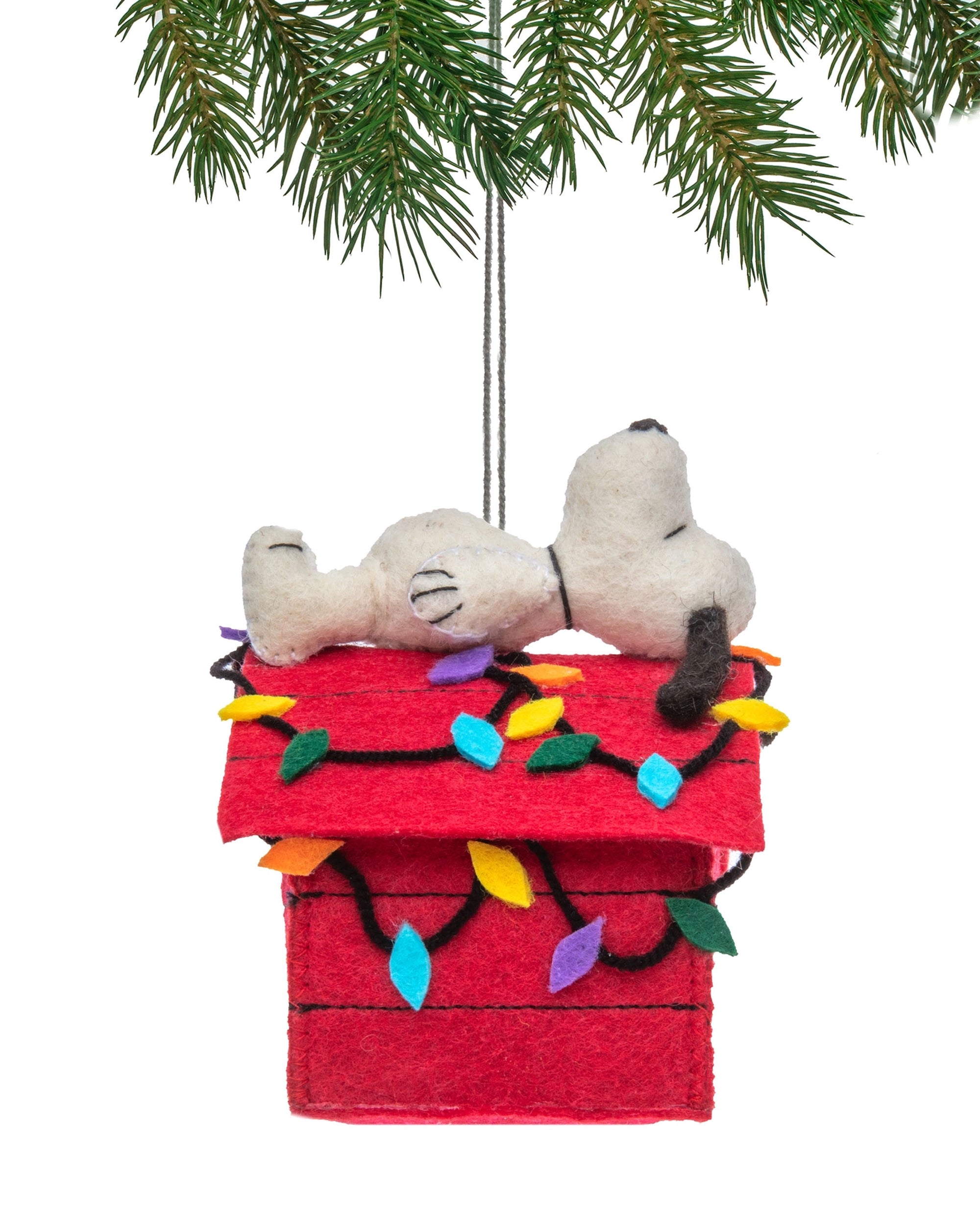 The Faire Snoopy Ornament features Snoopy lying atop his red doghouse with festive lights, hanging from a pine branch for a charming holiday decoration.