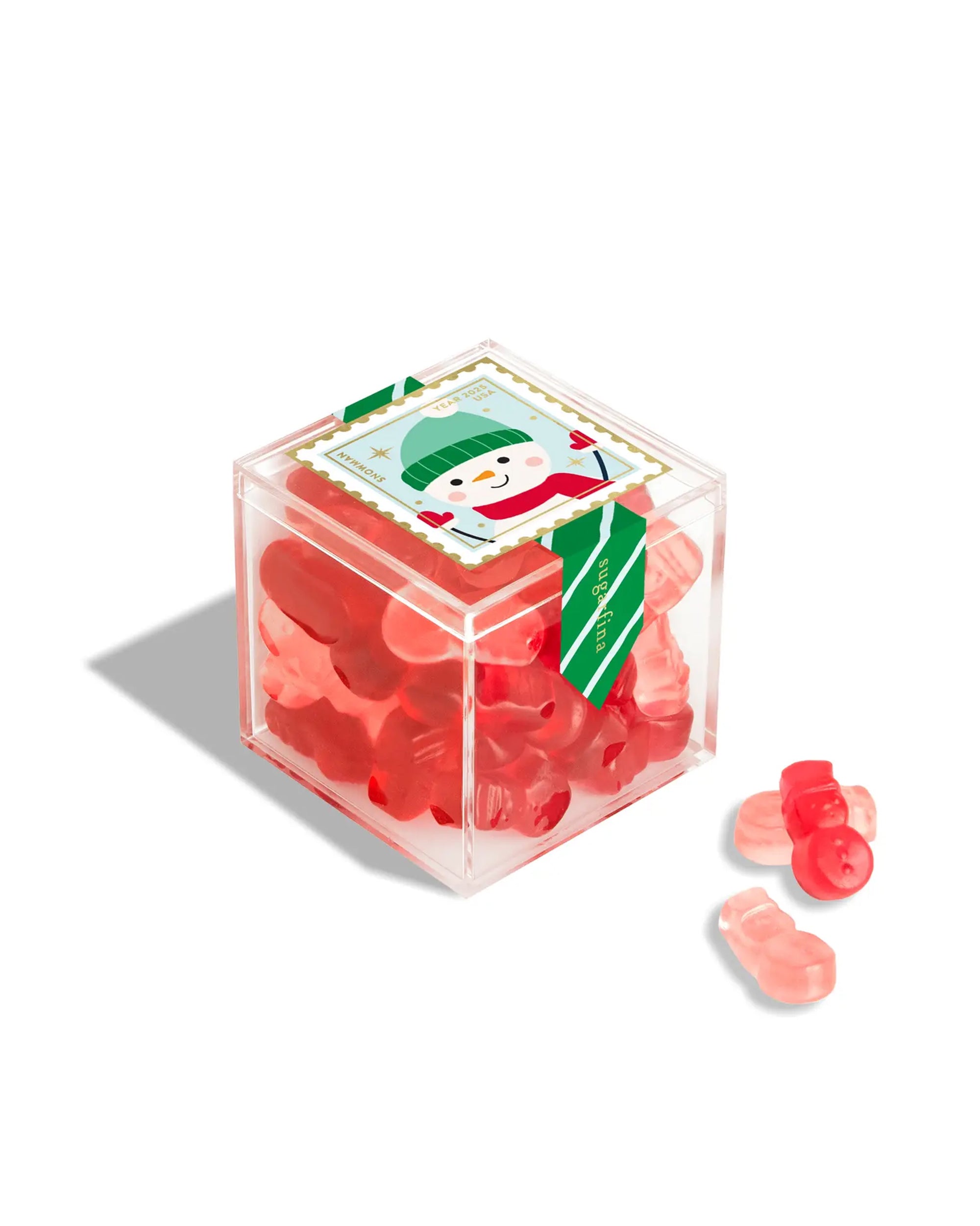 The Faire Christmas Candy Cube is a clear plastic box of red holiday candies, decorated with a festive snowman label and a few gummies displayed to the right of the box.