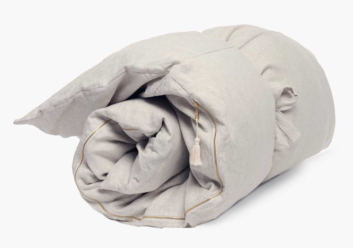 The Hedgehouse Throwbed, in light beige, is a neatly rolled cotton linen-blend comforter with a zipper and decorative tassel. Machine washable for easy care.