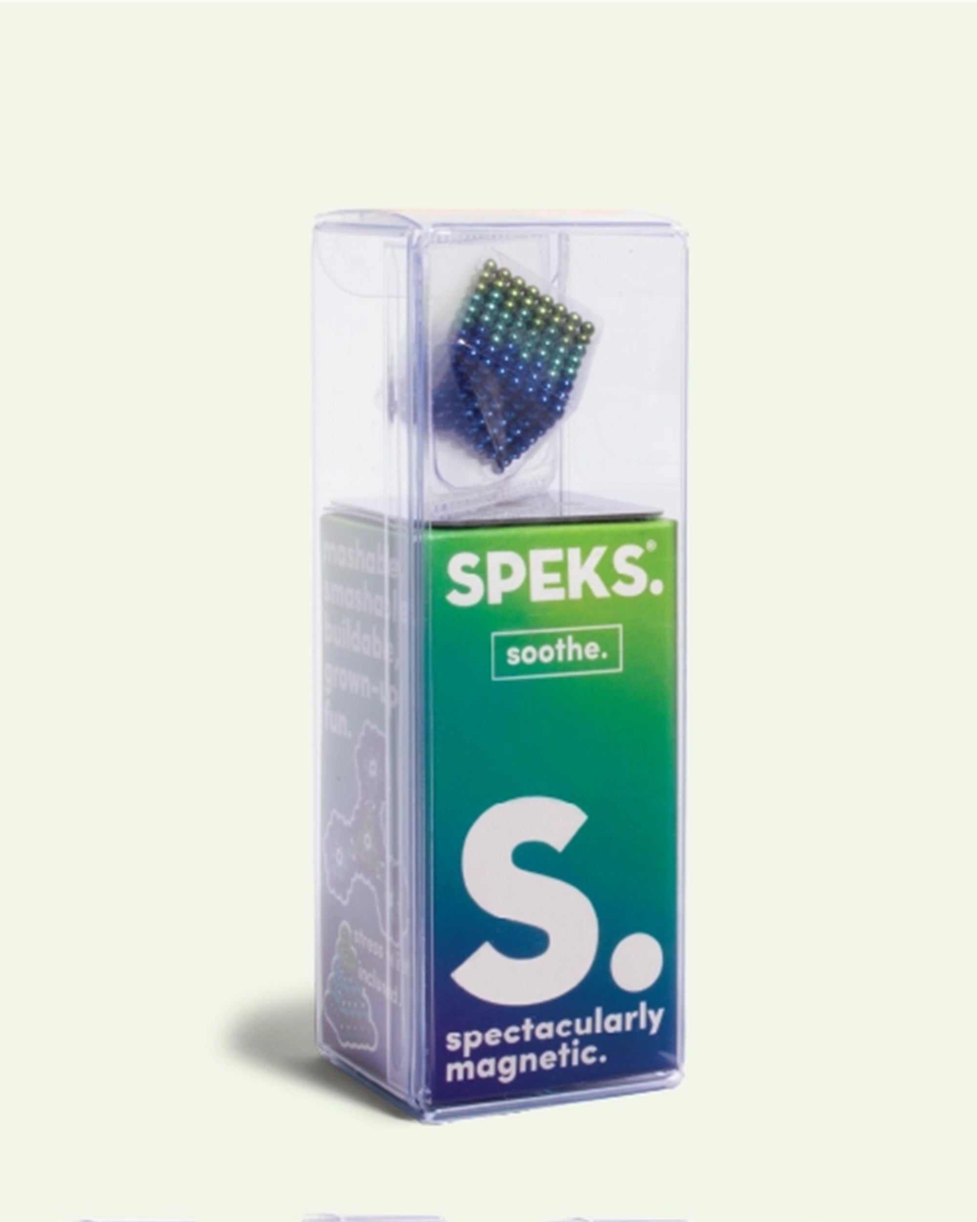 A clear plastic box contains Speks -512 Gradiante Soothe by Faire—small, colorful magnet balls in a cube. The packaging features "SPEKS.", "spectacularly magnetic.", and a green-blue gradient background. Great for stress relief and creativity.