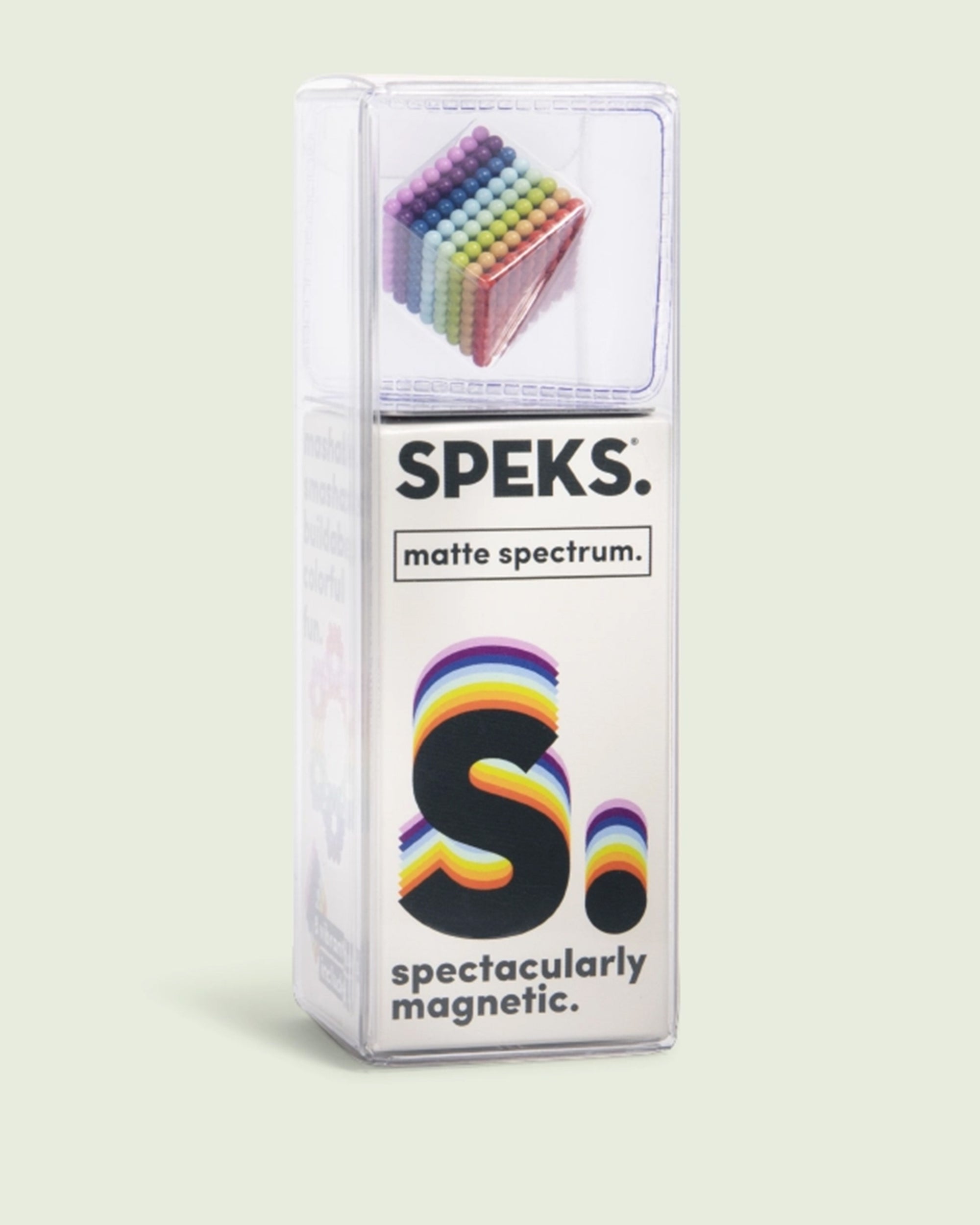 A clear, rectangular box labeled "Speks- Matte Spectrum" by Faire holds small, colorful magnetic balls stacked in a cube. The box says "S. spectacularly magnetic."—great for stress relief and building geometric shapes.