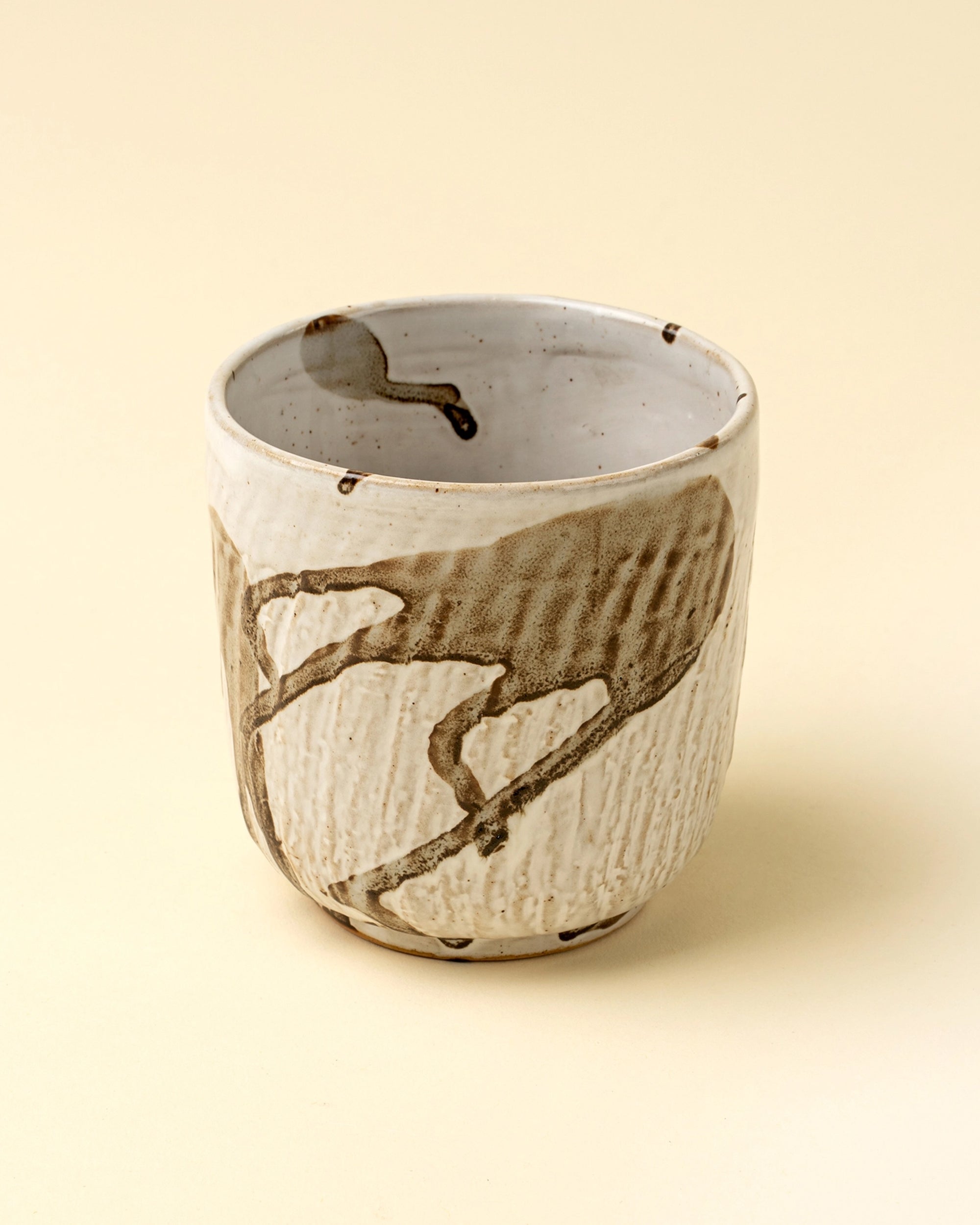 The Splash Porcelain Cup by Indaba features a handmade, textured off-white surface with abstract brown splash design, shown on a light beige background.