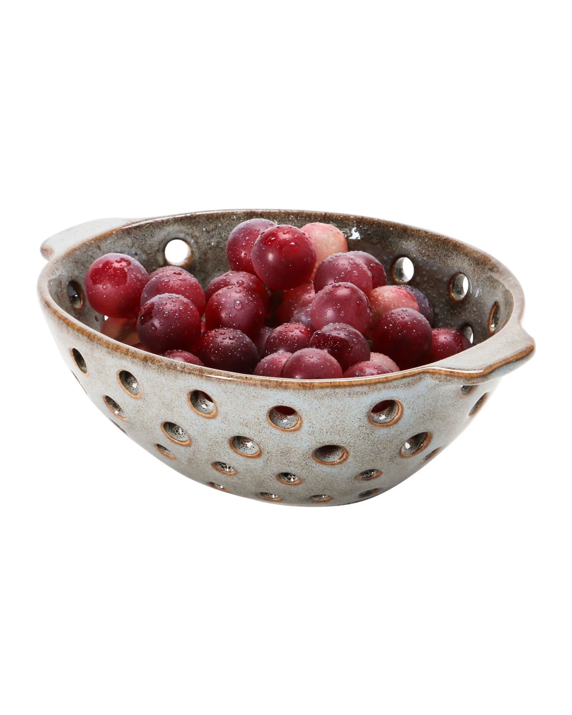 The Creative Co-op Berry Bowl with Glaze, featuring side handles and a reactive finish, displays fresh red grapes in style. Its pierced design makes it ideal for decorative use or rinsing fruit, shown here against a crisp white background.