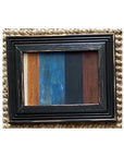 The STRIPES Framed Art by Tak Design is a small artwork featuring vertical stripes in cream, brown, blue, black, and dark brown hues, displayed on a textured beige woven surface.