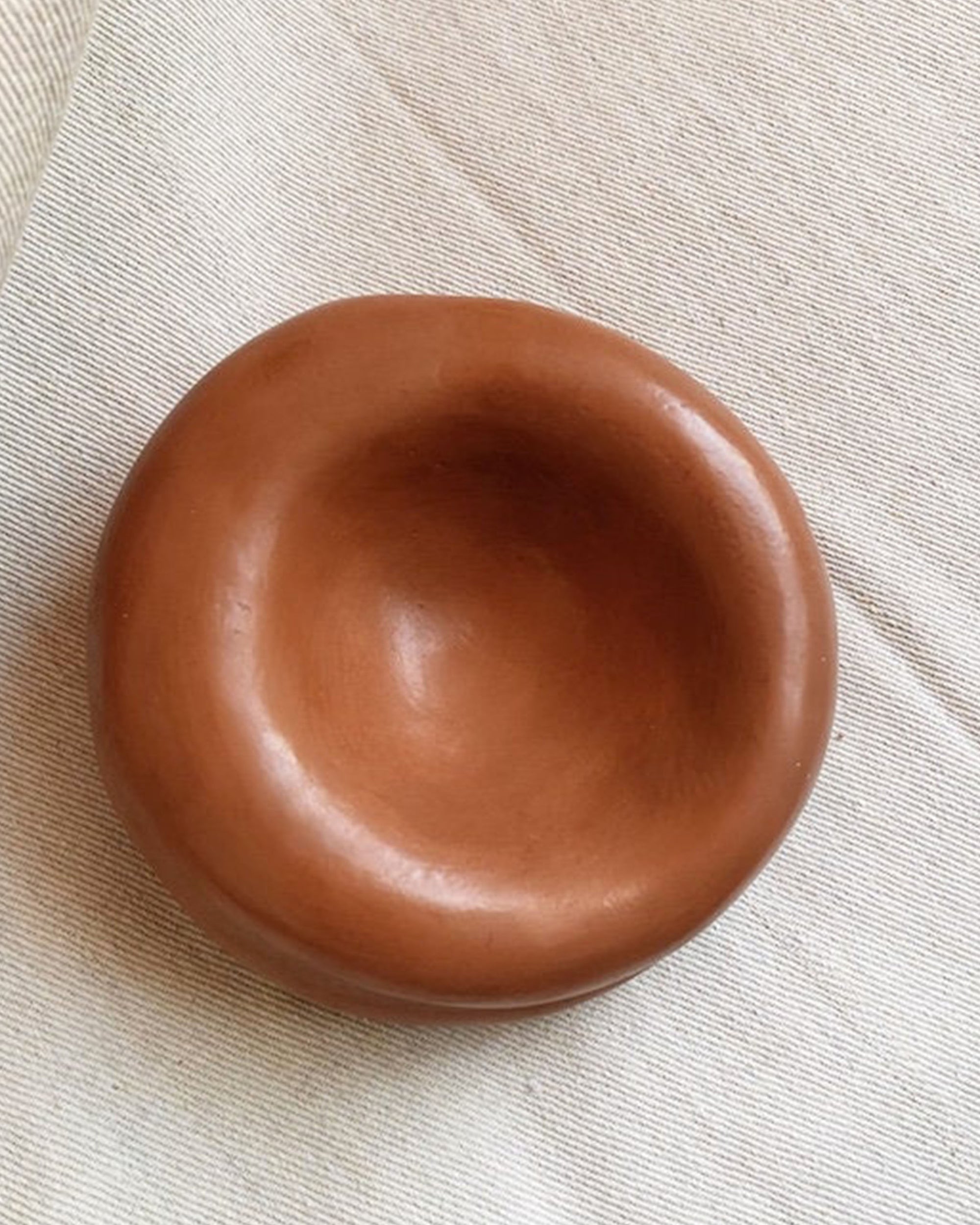 The Faire Sumo Pocket Concrete Bowl, featuring a small, round, and smooth handmade design with thick edges, rests on a textured light fabric background, adding wabi sabi charm to your décor.