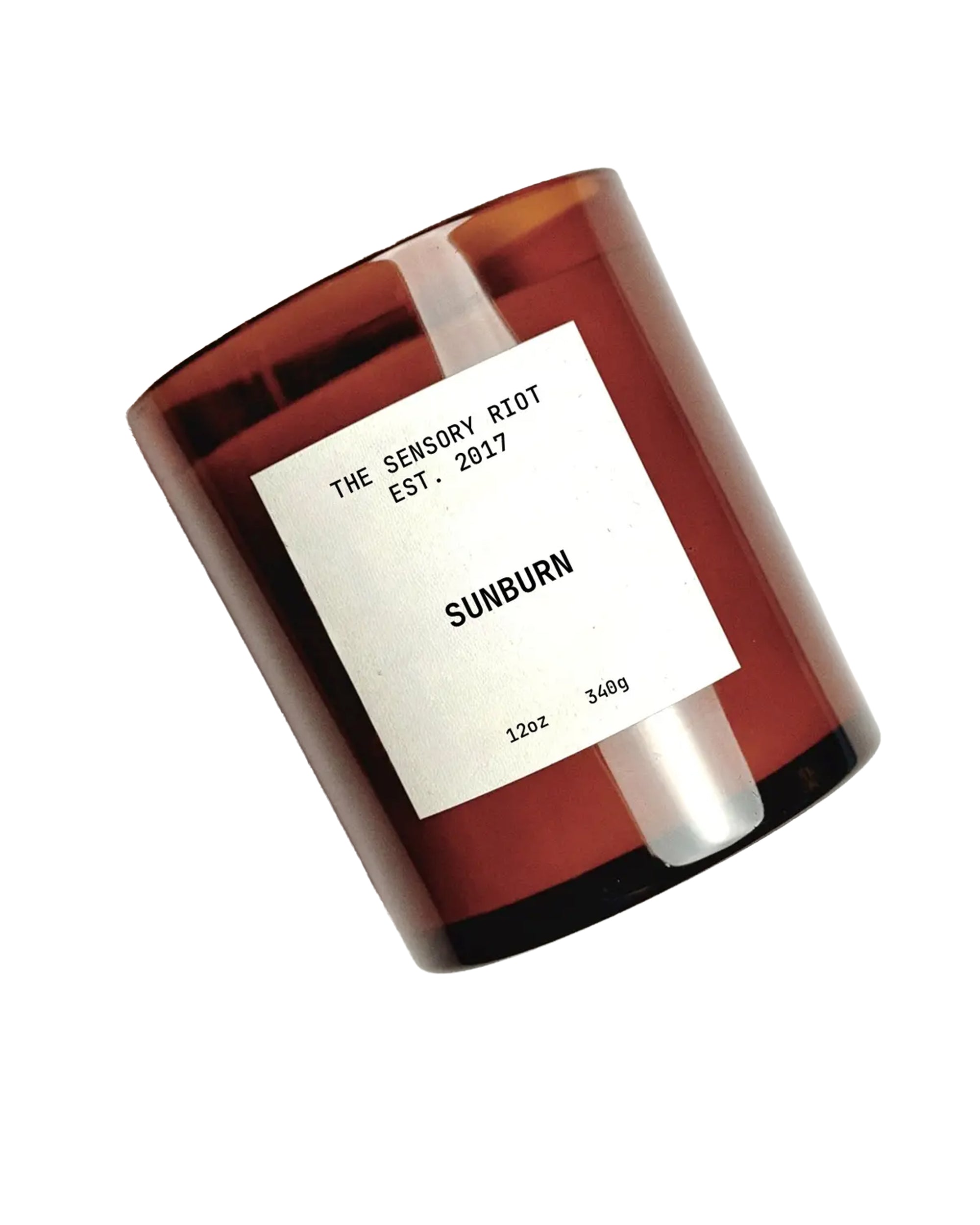 A brown glass jar labeled "Faire SUNBURN 12 oz" sits on a white background, featuring a clean burning scented soy wax candle.