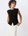 A woman wearing the SUNCOO PAGNI S/L button front top in black paired with a white skirt.