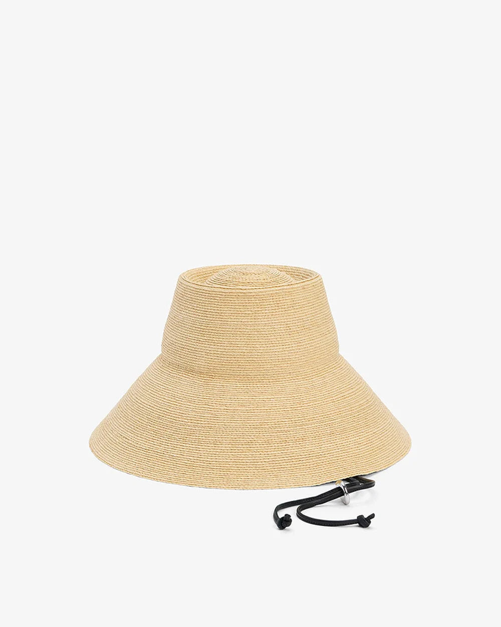 The Janessa Leone Suni Natural is a wide-brimmed raffia straw sun hat with a flat top and black adjustable chin strap, handcrafted in Madagascar and shown on a white background.