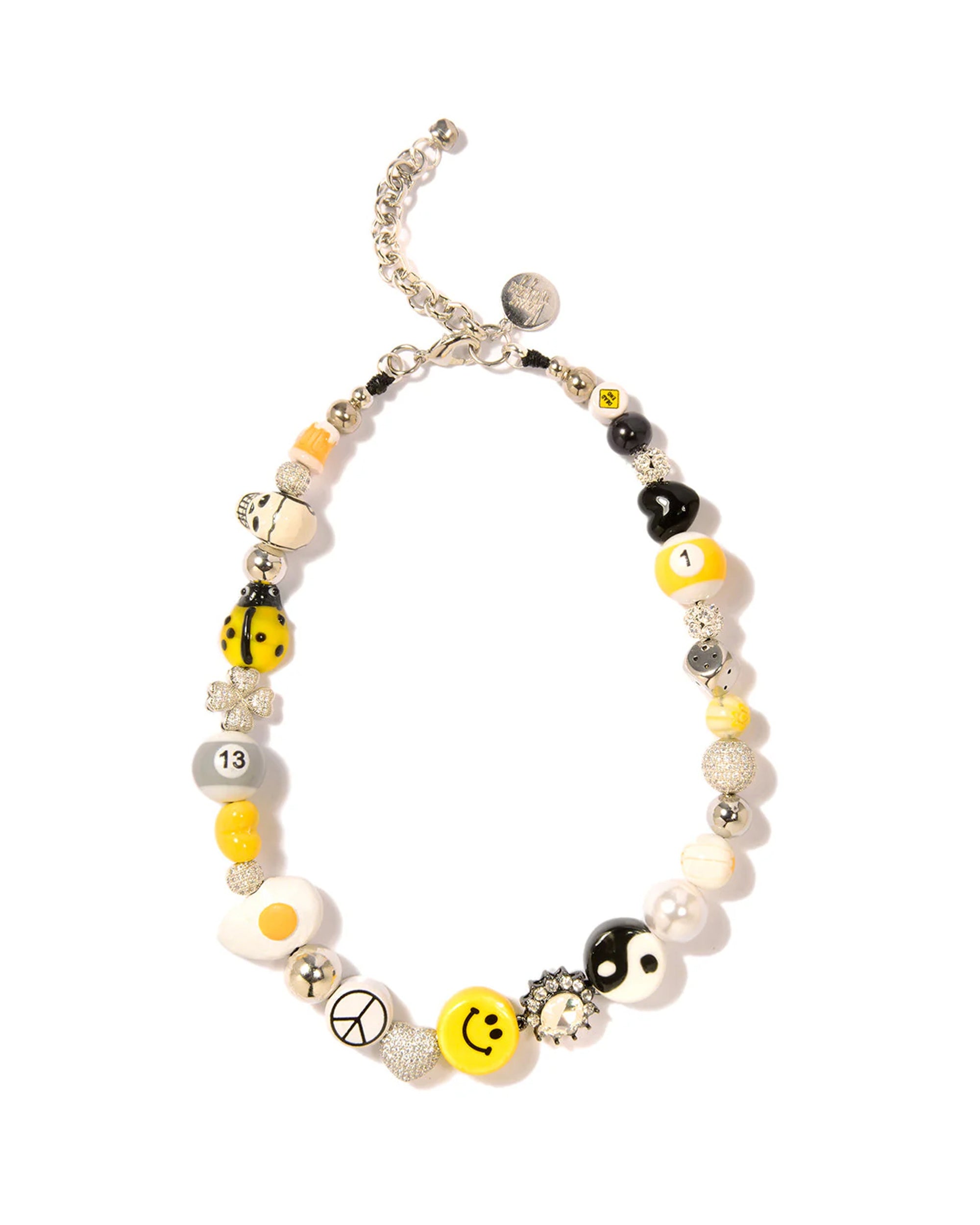 The Sunny Side Necklace 16" by Venessa Arizaga is a playful piece with silver, white, black, and yellow beads, smiley faces, yin-yang symbols, numbers, peace signs, fried egg motifs, and metallic accents on an adjustable silver chain.