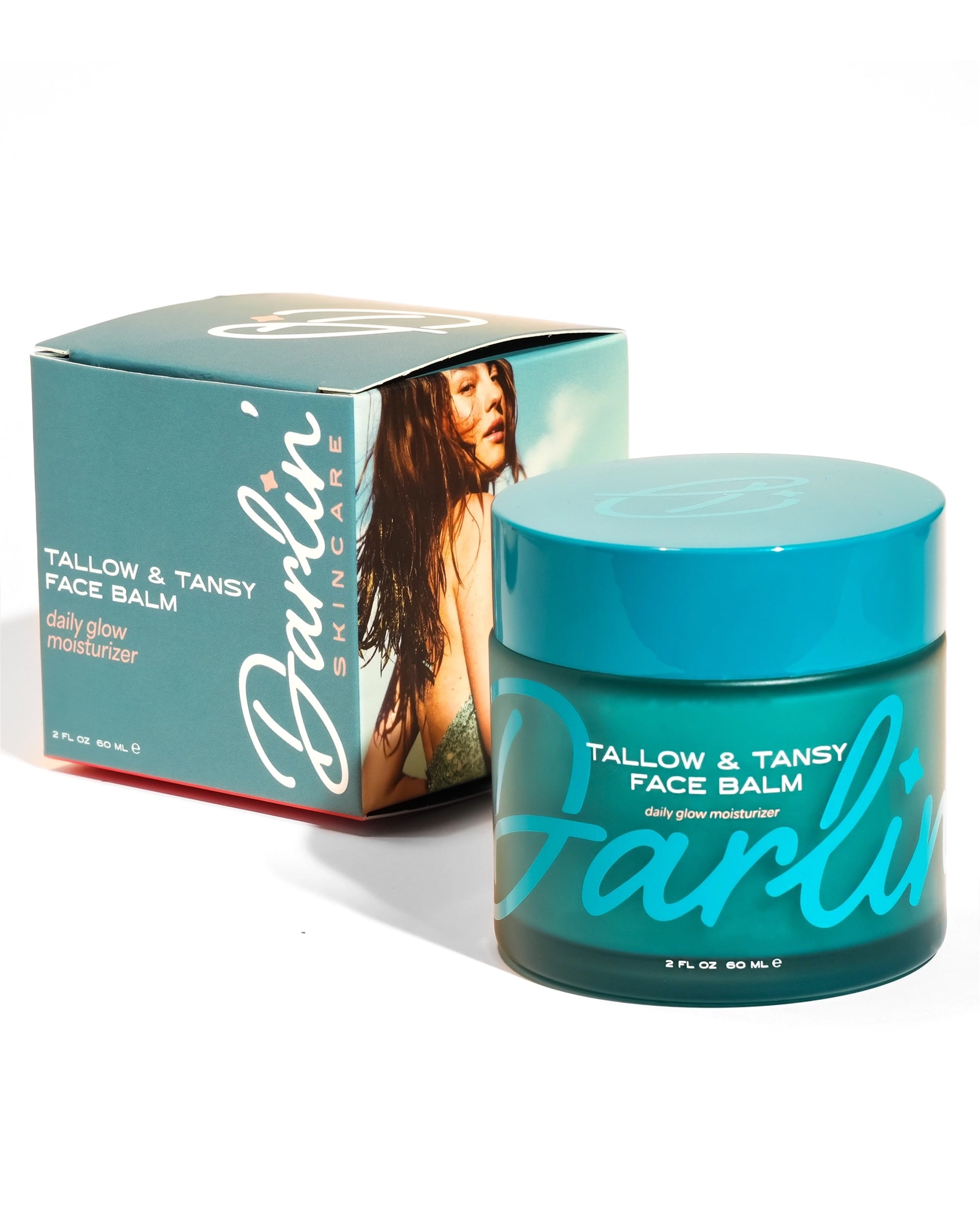 A teal jar of Faire Tallow Face Balm Moisturizer sits before its matching box, which features a woman's photo and product info. Made with grass-fed tallow, this daily moisturizer is ideal for acne-prone skin.