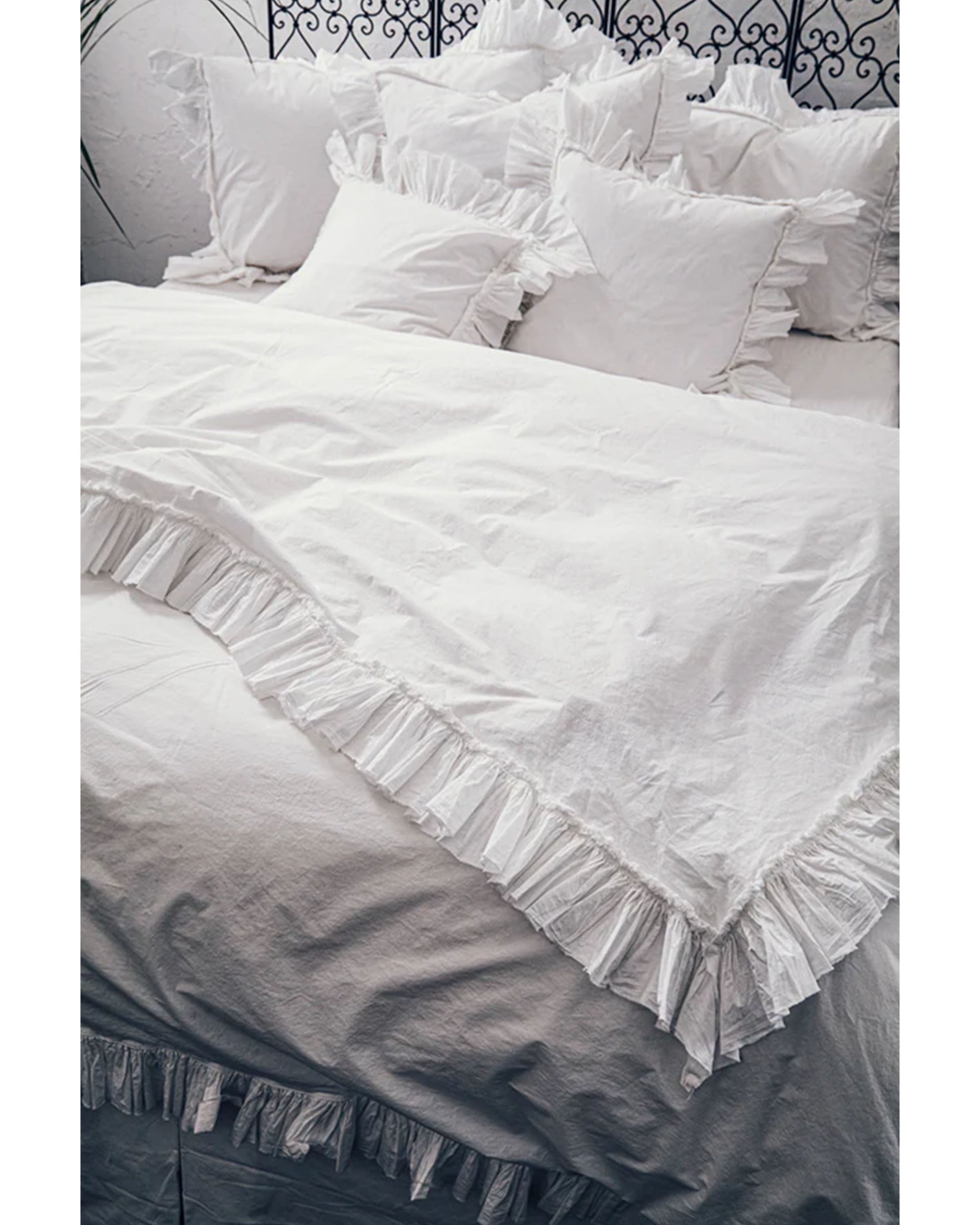 A neatly made bed features the Matteo Tat Cotton Duvet Cover with a white ruffle border and matching ruffled pillows, all set against a decorative wrought iron headboard.