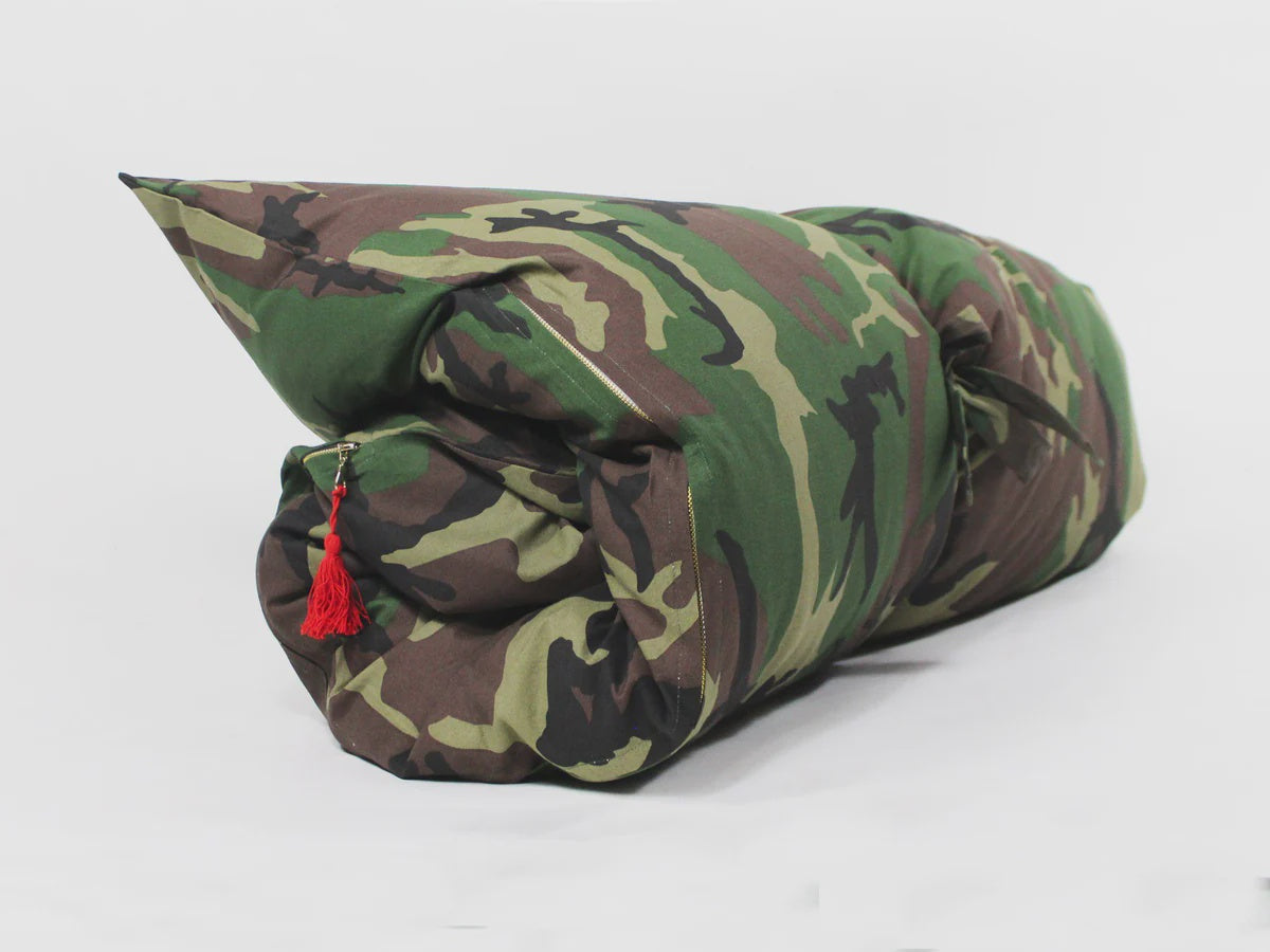The Hedgehouse Throwbed, a rolled-up military-style sleeping bag with a camouflage pattern and red tassel, reminiscent of outdoor cushions, is shown on a plain white background.