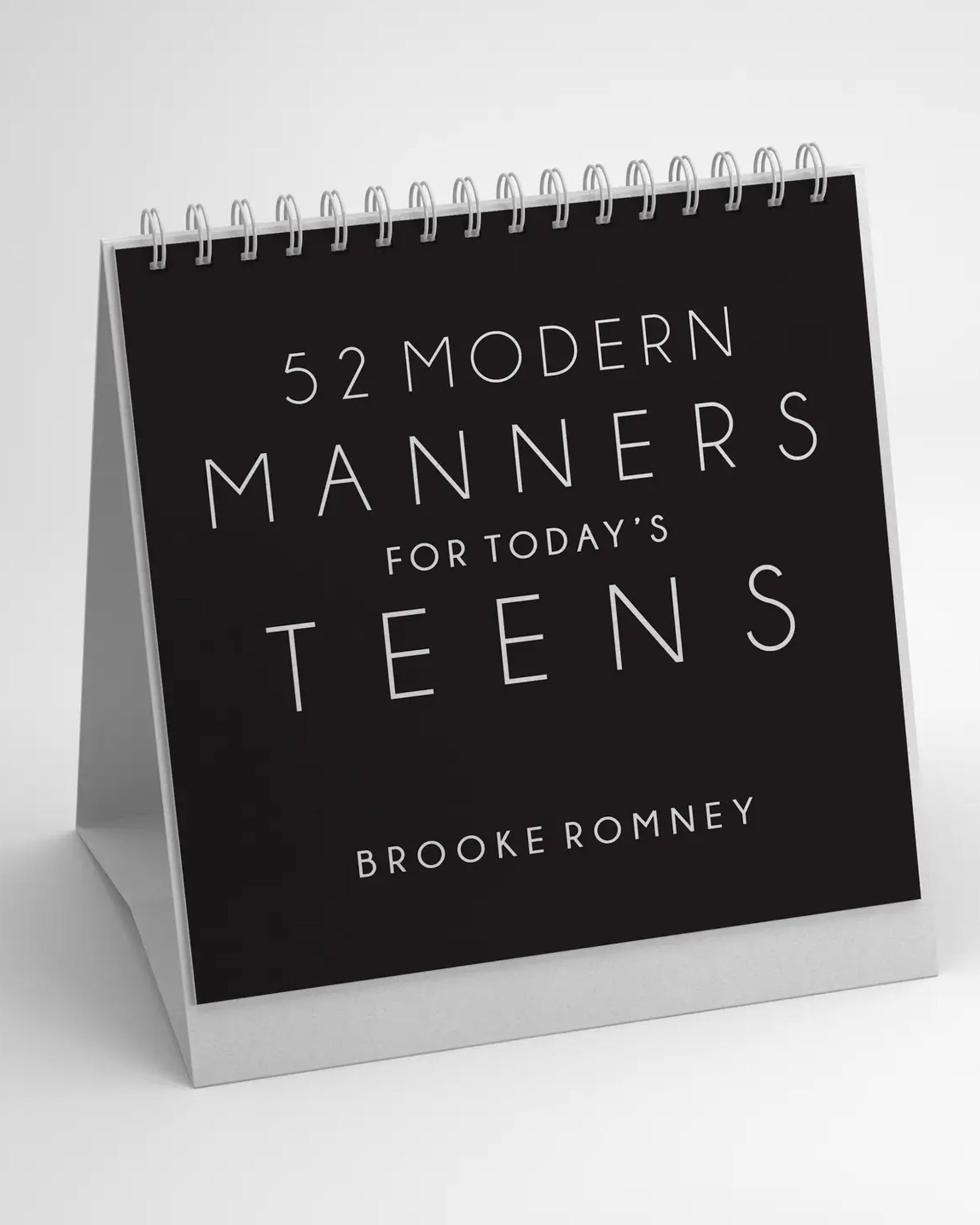 “52 Modern Manners” by Faire is a spiral-bound desk calendar designed to teach manners and social skills, featuring a minimalist black cover with white text.