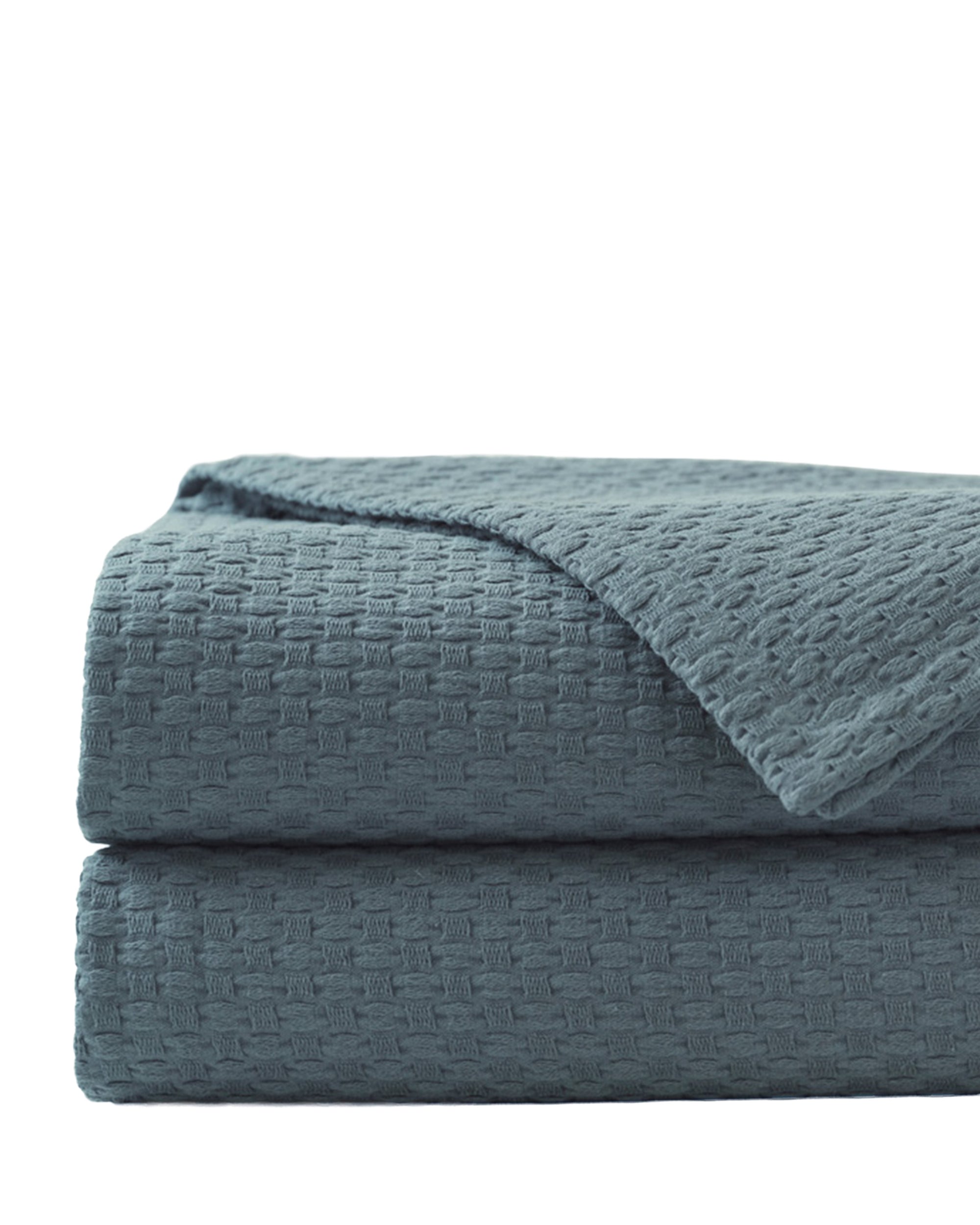 The Tegan Matelasse Coverlet by Eastern Accents, featuring a blue waffle-weave texture and mitered hem, is neatly folded and stacked against a plain white background.