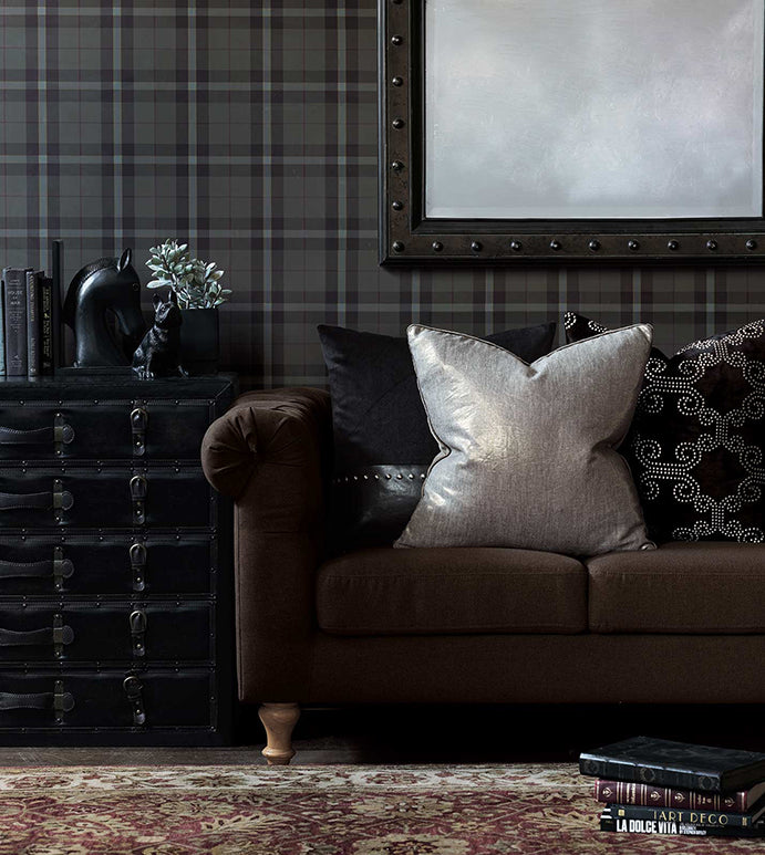 A sophisticated living room features a brown sofa with plush cushions, including an Eastern Accents Leonis Linen 22x22&quot; pillow in metallic linen, a studded black side cabinet adorned with books and a decorative horse head, framed wall art, and a richly patterned area rug. The decor exudes a blend of vintage and contemporary style.