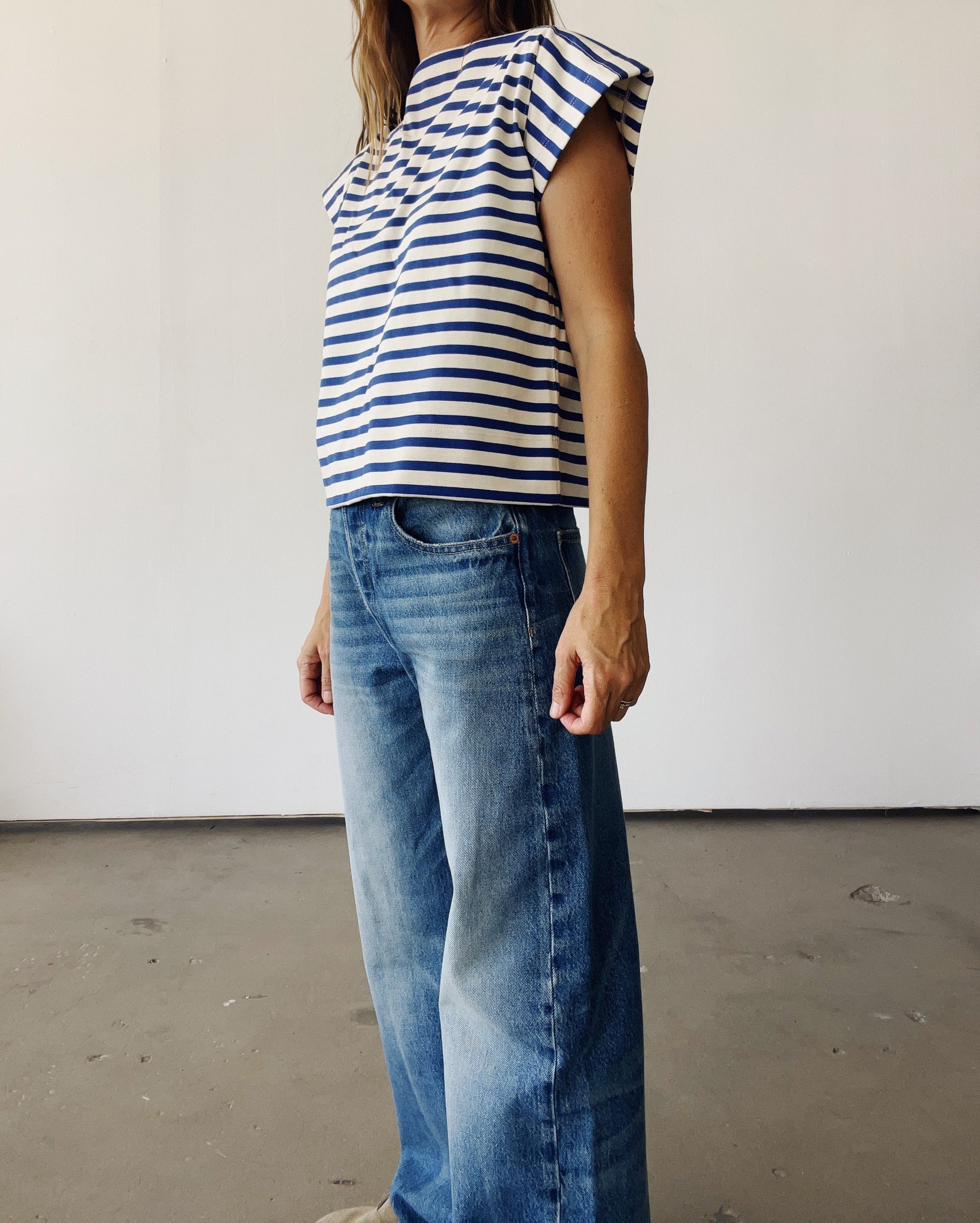 A person models The Sailor Shirt by Hey Gang—blue and white striped—paired with wide-leg blue jeans, standing against a plain, light-colored wall with their face not shown.