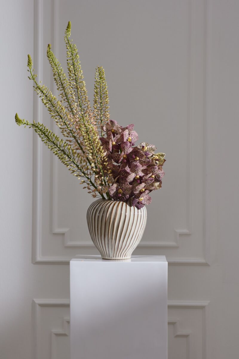 Tomar Vase by Accent Decor with tall green stems and purple spotted flowers on a sleek white pedestal.
