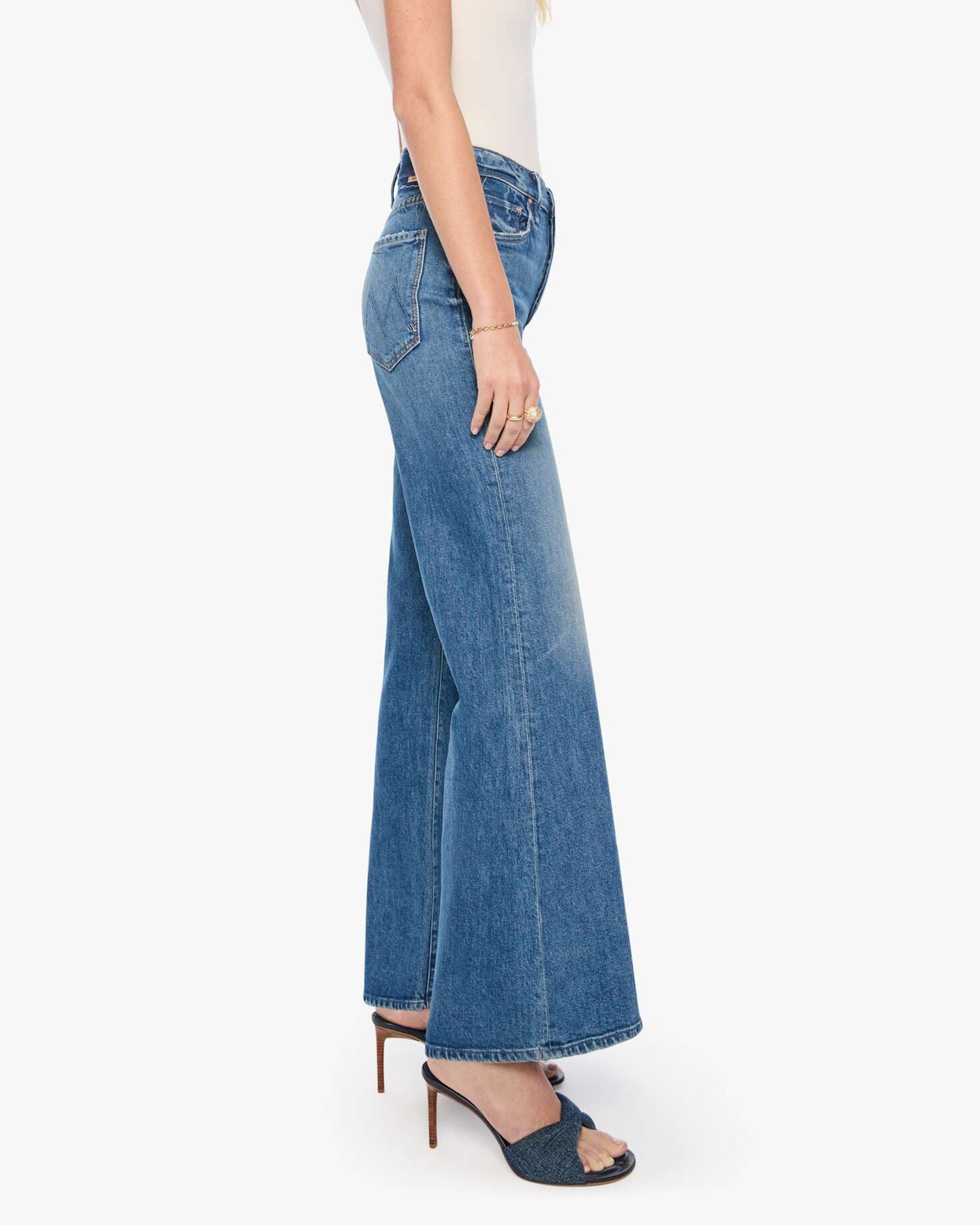 Mother’s The Tomcat Roller Sneak jeans in blue denim, styled with a white top and heeled sandals, side view.