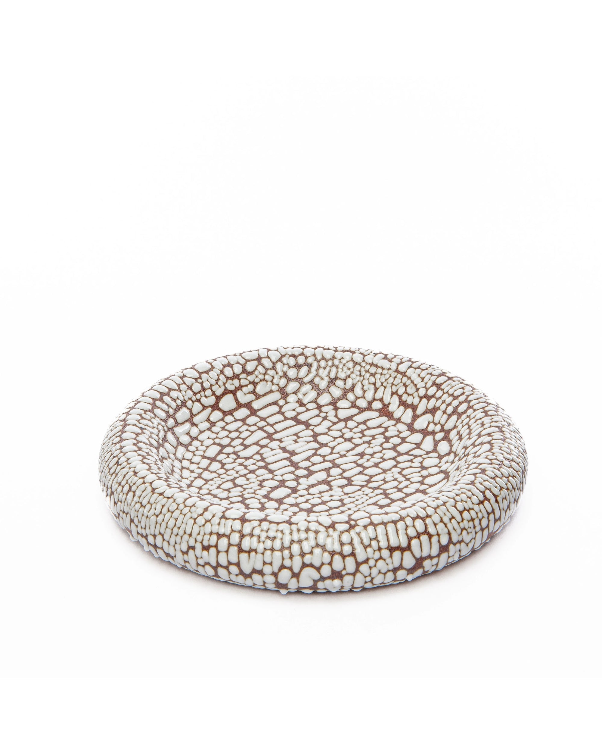 The Faire Torus Bowl is a round, shallow piece featuring textured irregular white shapes on a brown background, resembling mosaic tiles. A striking decor object or stylish catch-all, it stands out beautifully against any plain white surface.