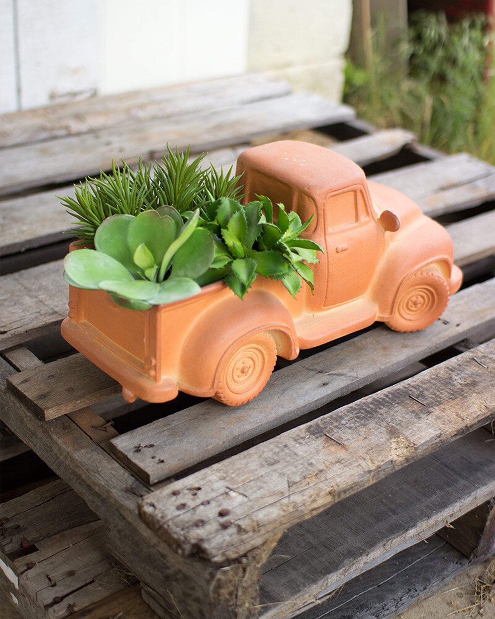 The CTR200 Truck Planter by Kalalou, Inc is a ceramic planter shaped like a vintage pickup truck, filled with lush succulents and displayed outdoors on a rustic wooden pallet.