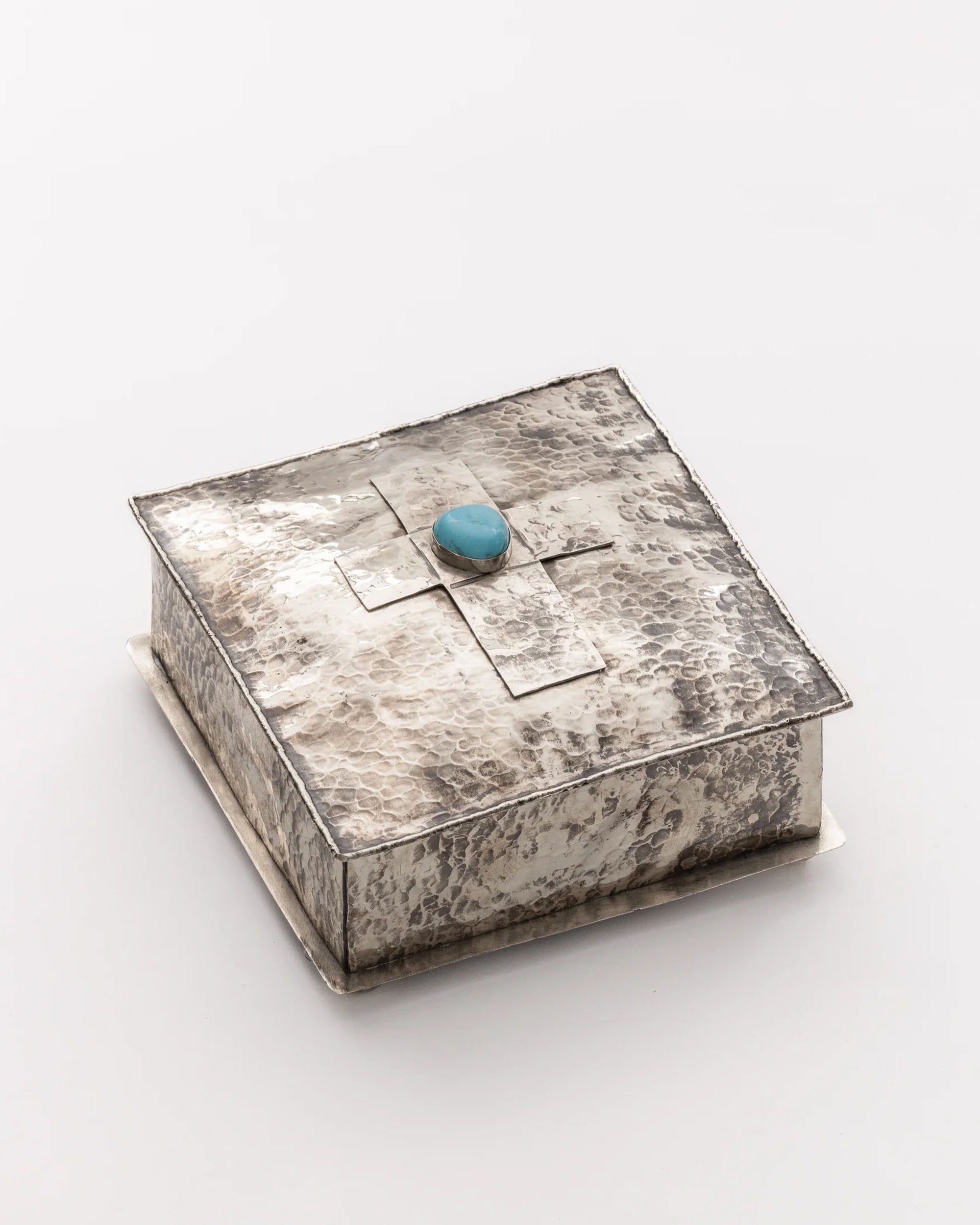 The 75-T-SL 6x6 SQ Silver Box w/ Dimples Cross by J Alexander Rustic Silver is a square, rustic hammered silver box with a raised cross and turquoise stone, ideal for Southwestern home decor.