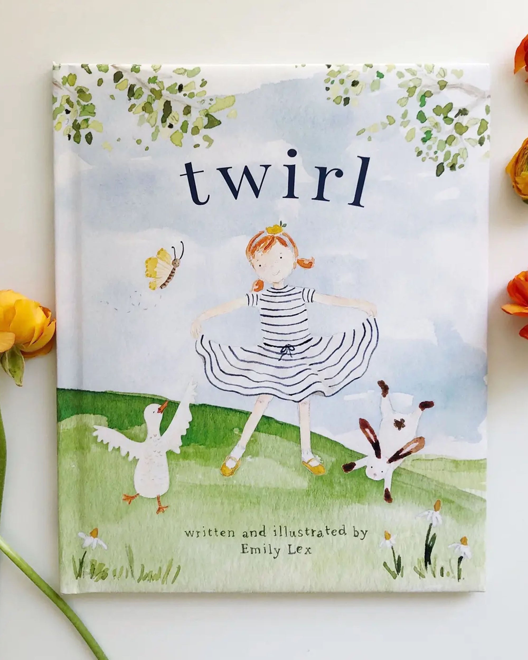 The cover of the TWIRL BOOK by Faire features a girl in a striped dress dancing on grass with a duck, dog, and butterfly nearby under leafy branches, while orange flowers decorate the image’s edges.
