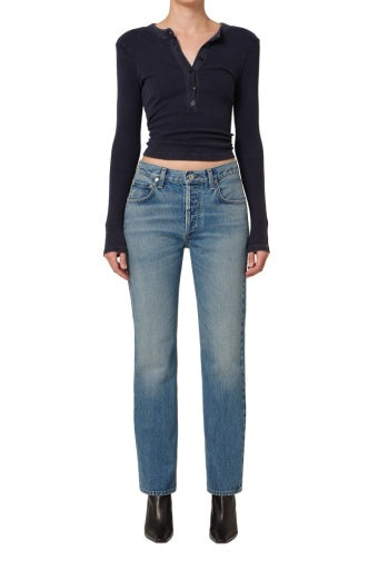 A person stands facing forward against a white background wearing a long-sleeve navy button-up crop top, the Citizens Of Humanity/AGOLDE Savannah Cigarette Jean in Patina, and black ankle boots.