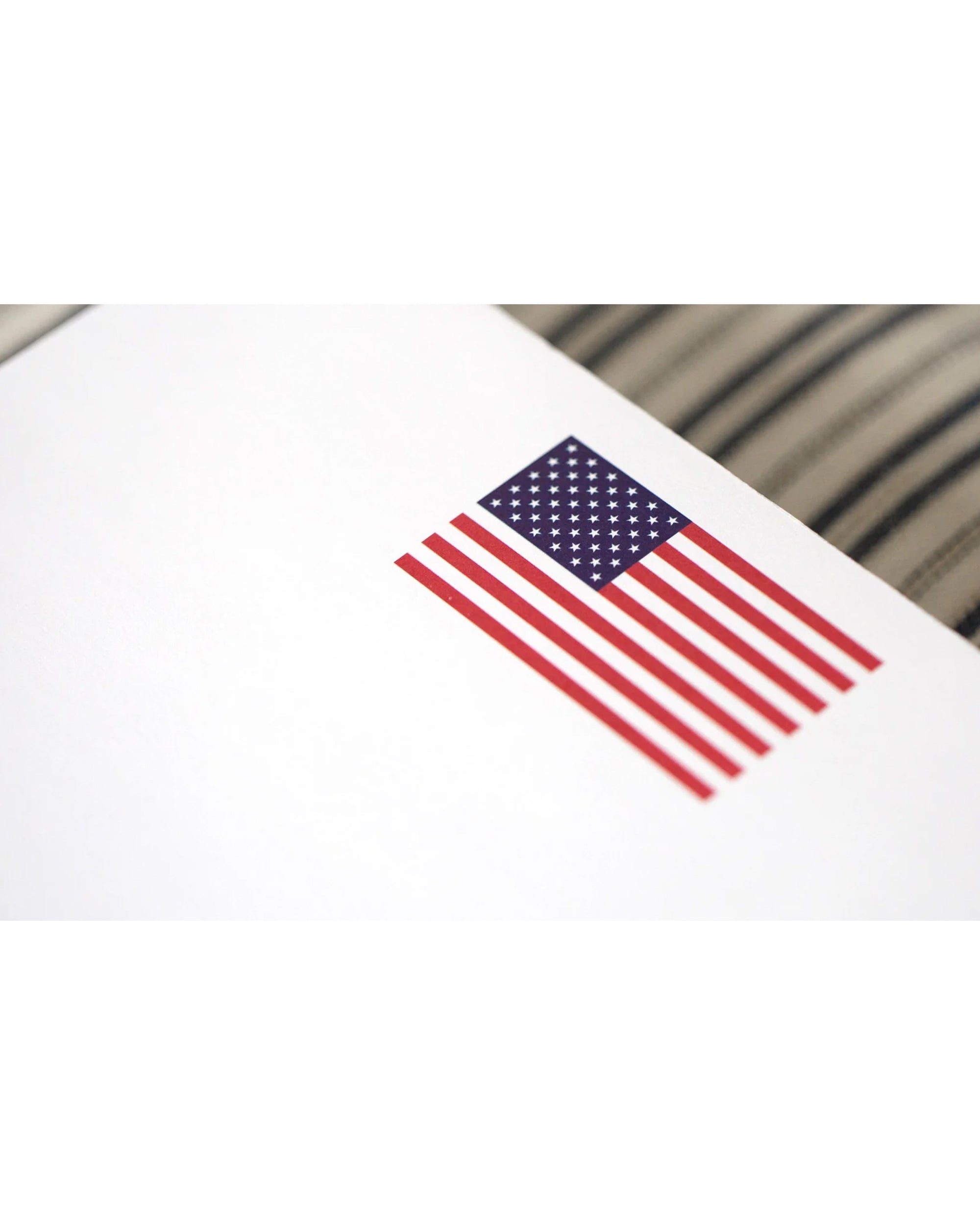 The Black Ink US Flag NP notepad features a small United States flag with a blurred, striped background on luxurious quality paper—an ideal gift for veterans.