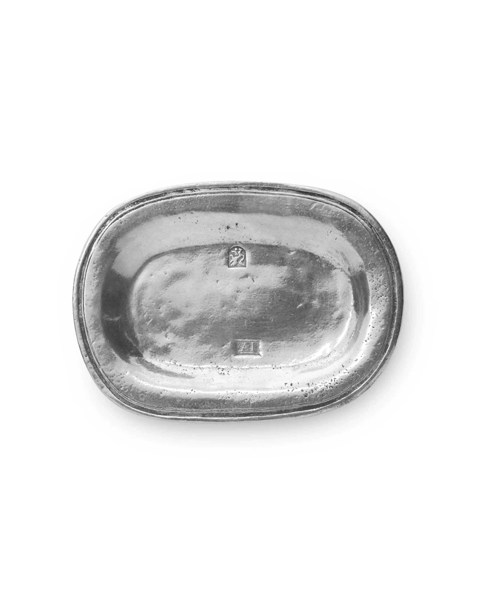 The Faire Vintage Bedside Tray is an oval, silver tray handcrafted from Italian pewter, featuring a subtly raised edge and two small rectangular hallmarks in the center. Shown on a white background, this elegant piece doubles as a stylish jewelry organizer or vintage accent for your bedside table.