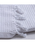 A close-up of the Faire Waffle Hand Towel, made from white Turkish cotton with a waffle weave and decorative twisted fringe tassels, displayed on a white surface.