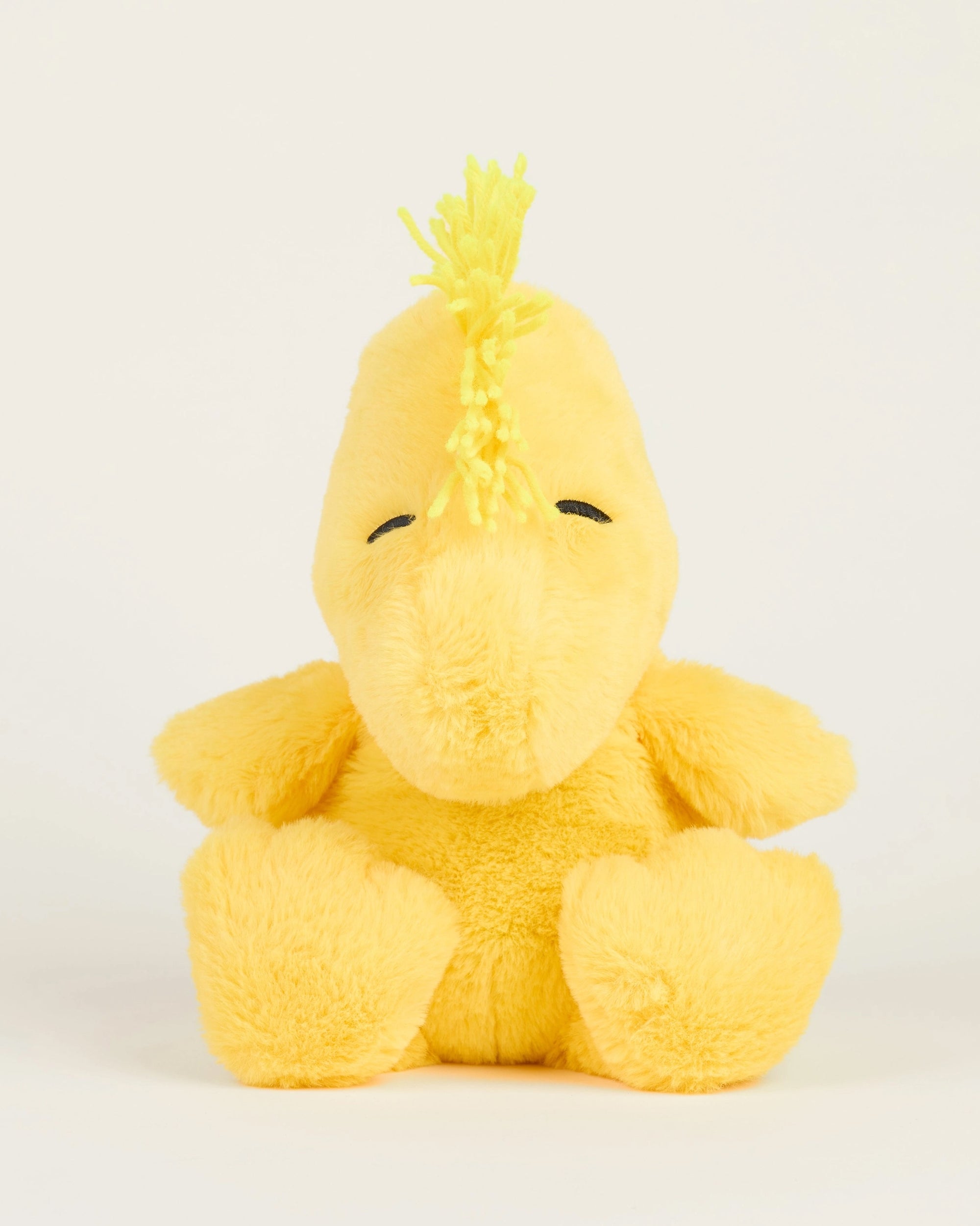 The Woodstock Warmies by Warmies/Intelex is a yellow microwavable plush toy with closed embroidered eyes and a tuft of yellow yarn hair, offering soothing warmth and comfort when heated.