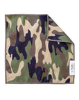 A square waffle weave microfiber washcloth from Faire, featuring a green, brown, tan, and black camouflage pattern with a stitched border. Highly absorbent and eco-friendly. One corner is slightly folded over.