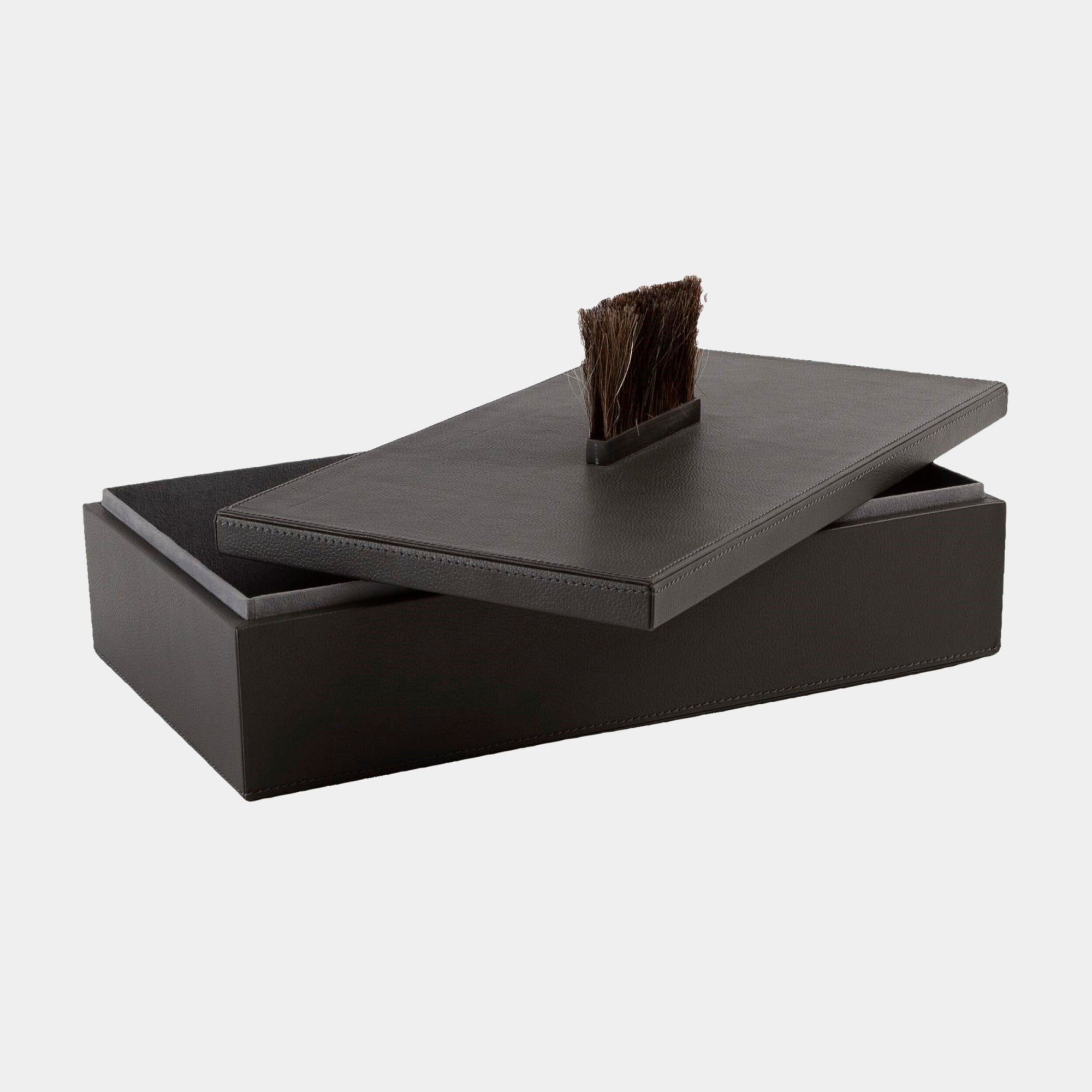 The Harrington Box Graphite Leather by Global Views is a rectangular, black top grain leather box with a matching lid featuring a brown bristle brush handle. The angled lid reveals the empty interior.