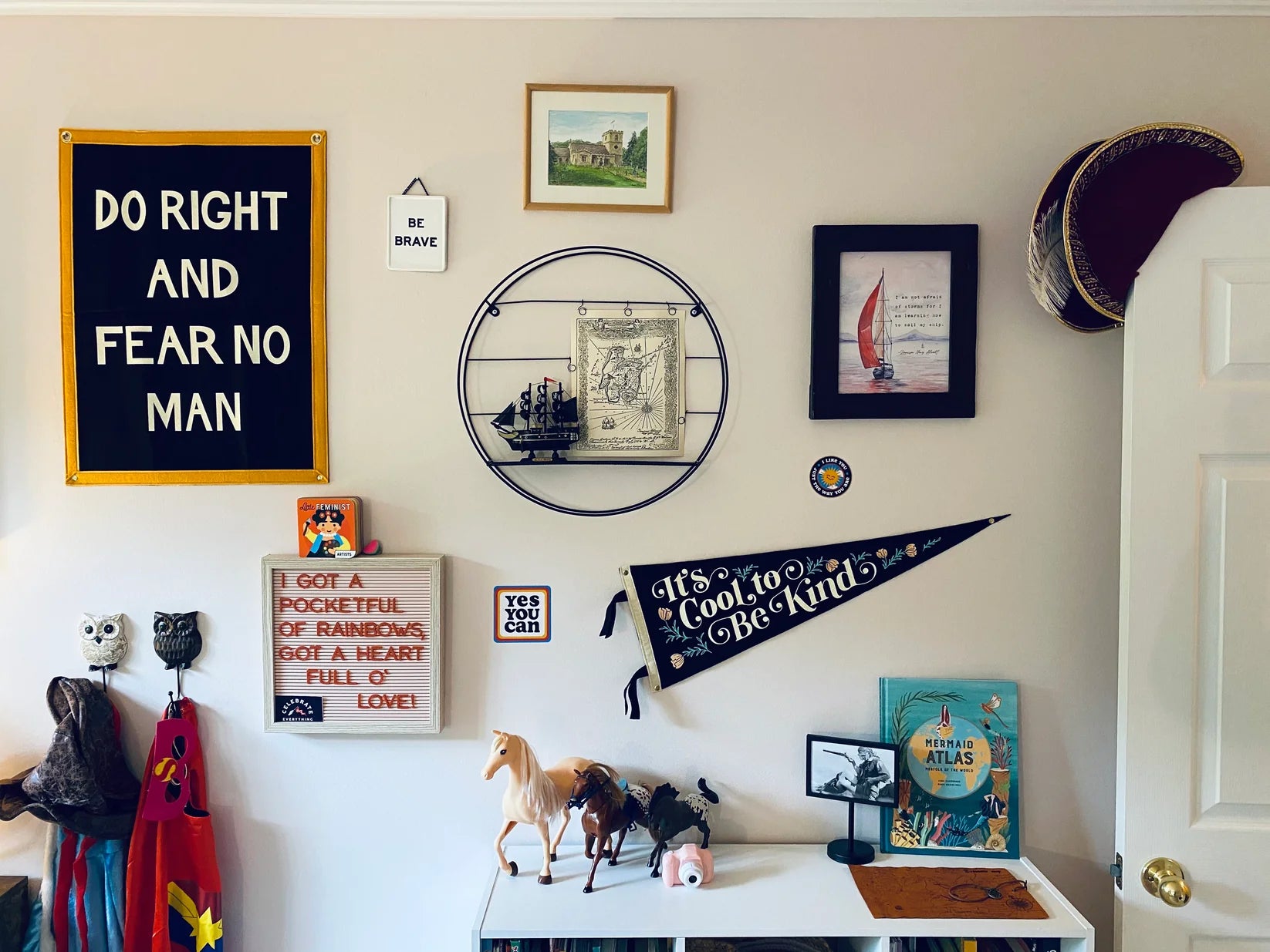 A wall featuring the Oxford Pennant "Do Right and Fear No Man" 18x24 camp flag, framed art, a ship model, a pirate hat, and a shelf with books, horse figurines, and an owl creates a whimsical, adventurous atmosphere.