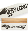 The "Long Safety Matches" by Faire come in a rectangular box featuring an illustrated dachshund and the words "VERY LONG MATCHES." Inside, extra-long wooden matches with white tips are neatly arranged.