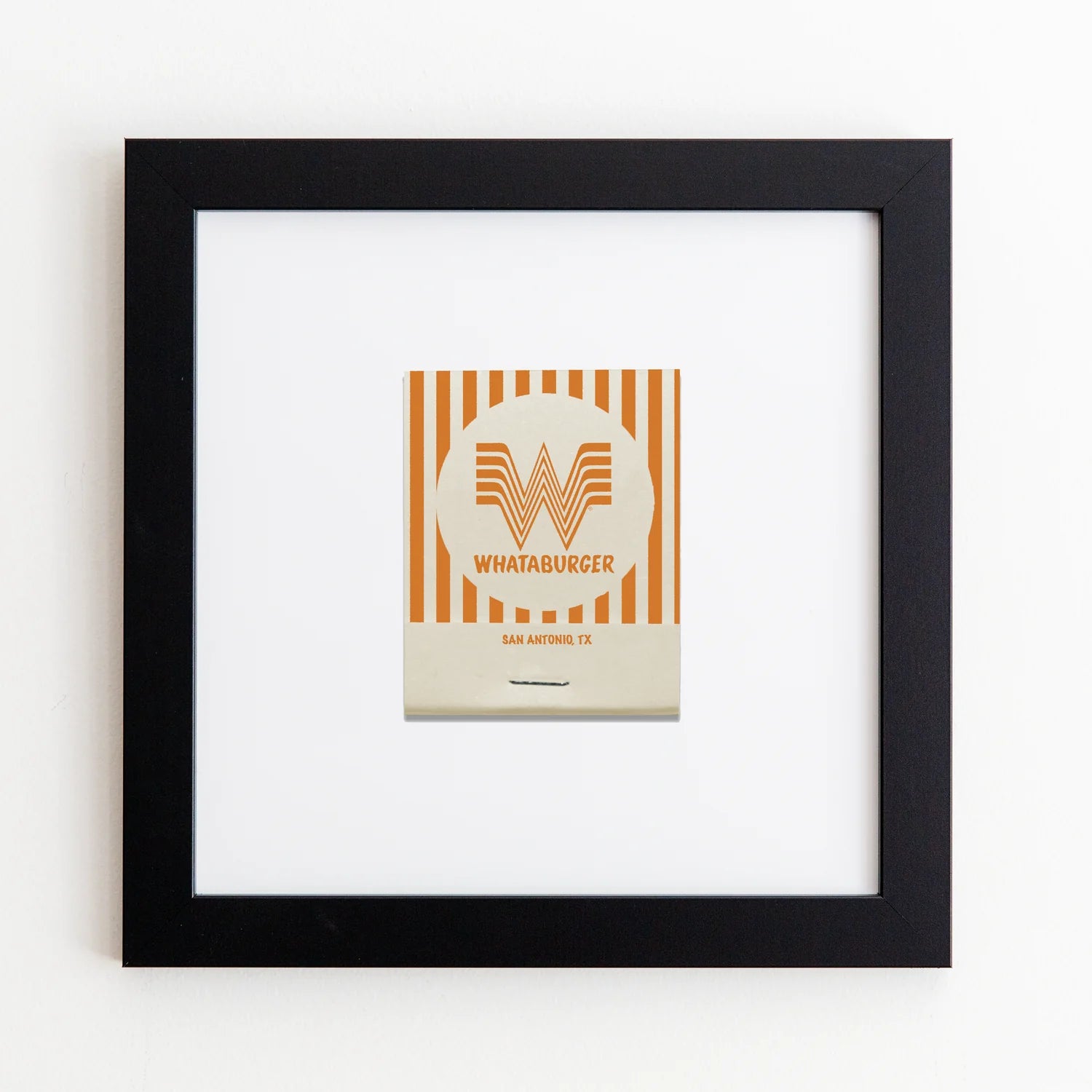 A framed Art Square Black Frame of Whataburger&#39;s logo with orange and white stripes and a stylized &quot;W&quot; in the center, titled &quot;San Antonio, TX,&quot; displayed on a white wall by Match South.