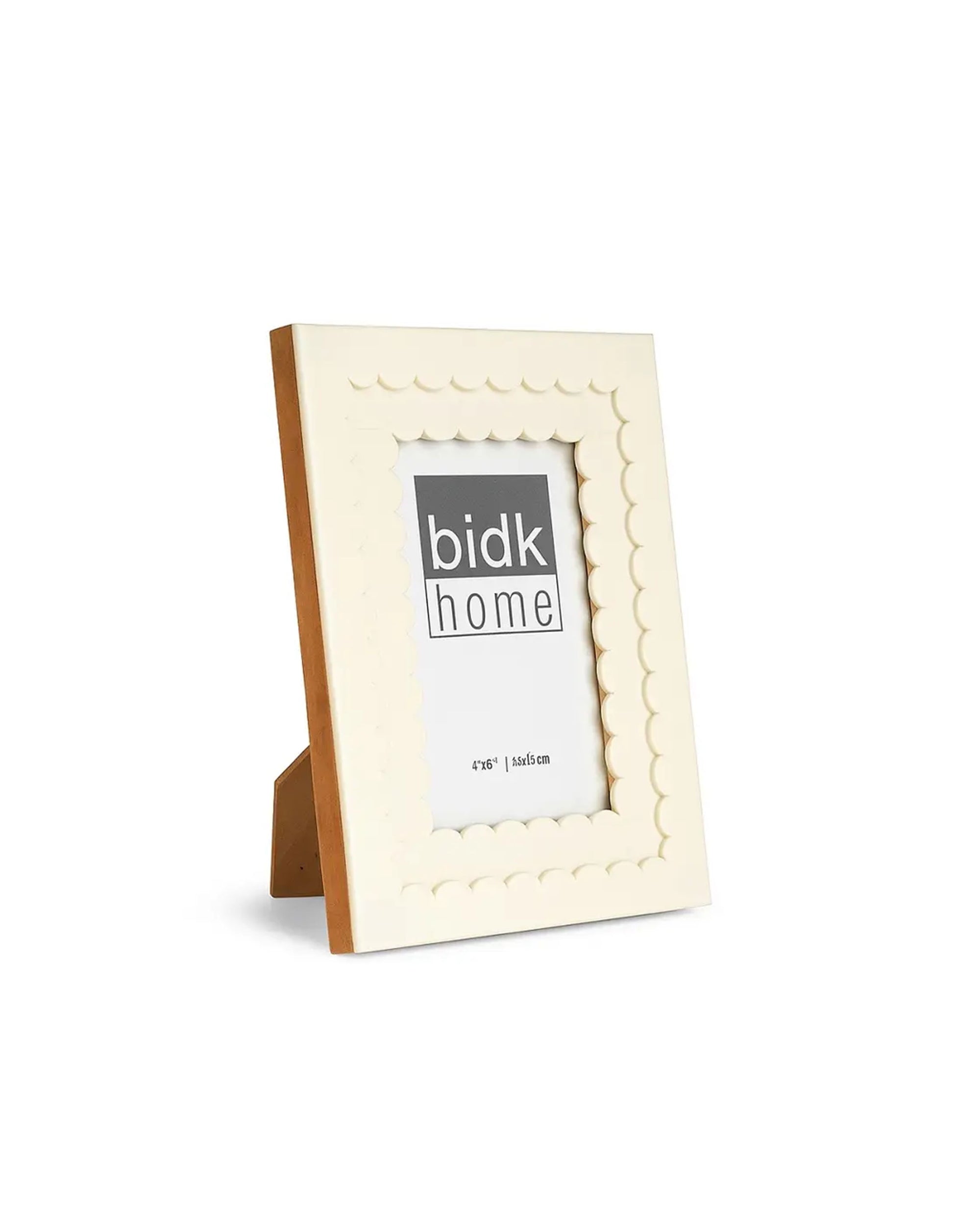 The 705141 4x6 Floral Resin Frame by BIDK Home features a cream color, scalloped edges, and sleek design with a wooden stand. Ideal for home decor, it holds a 4x6 photo and is displayed at an angle on a white background.
