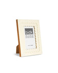 The 705141 4x6 Floral Resin Frame by BIDK Home features a cream color, scalloped edges, and sleek design with a wooden stand. Ideal for home decor, it holds a 4x6 photo and is displayed at an angle on a white background.