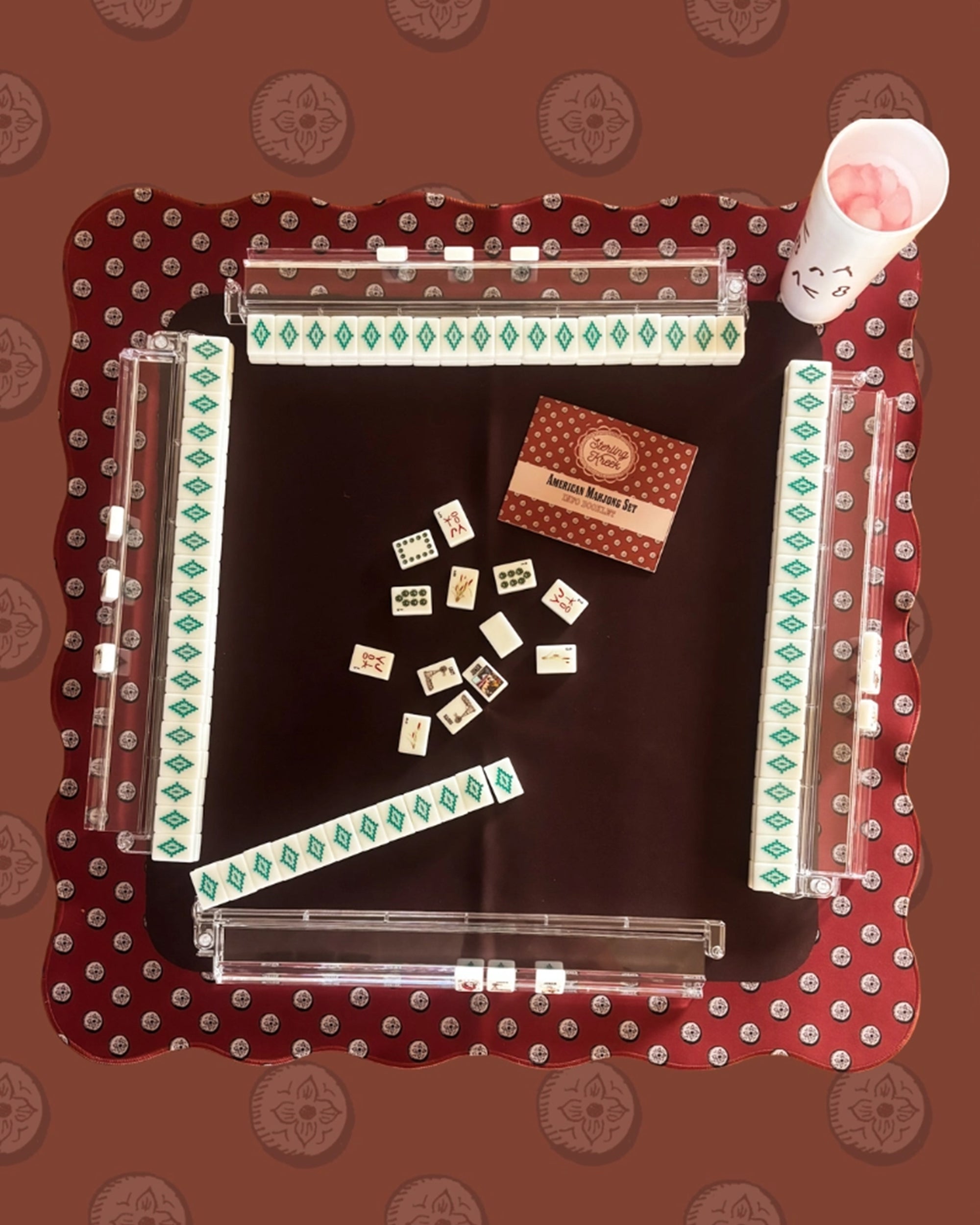 The Faire Wild West Mahjong SET includes tiles, 4 racks, a bag, and a maroon patterned mat for game setup; rule book and accessories also featured.