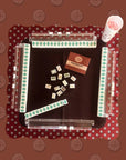 The Faire Wild West Mahjong SET includes tiles, 4 racks, a bag, and a maroon patterned mat for game setup; rule book and accessories also featured.