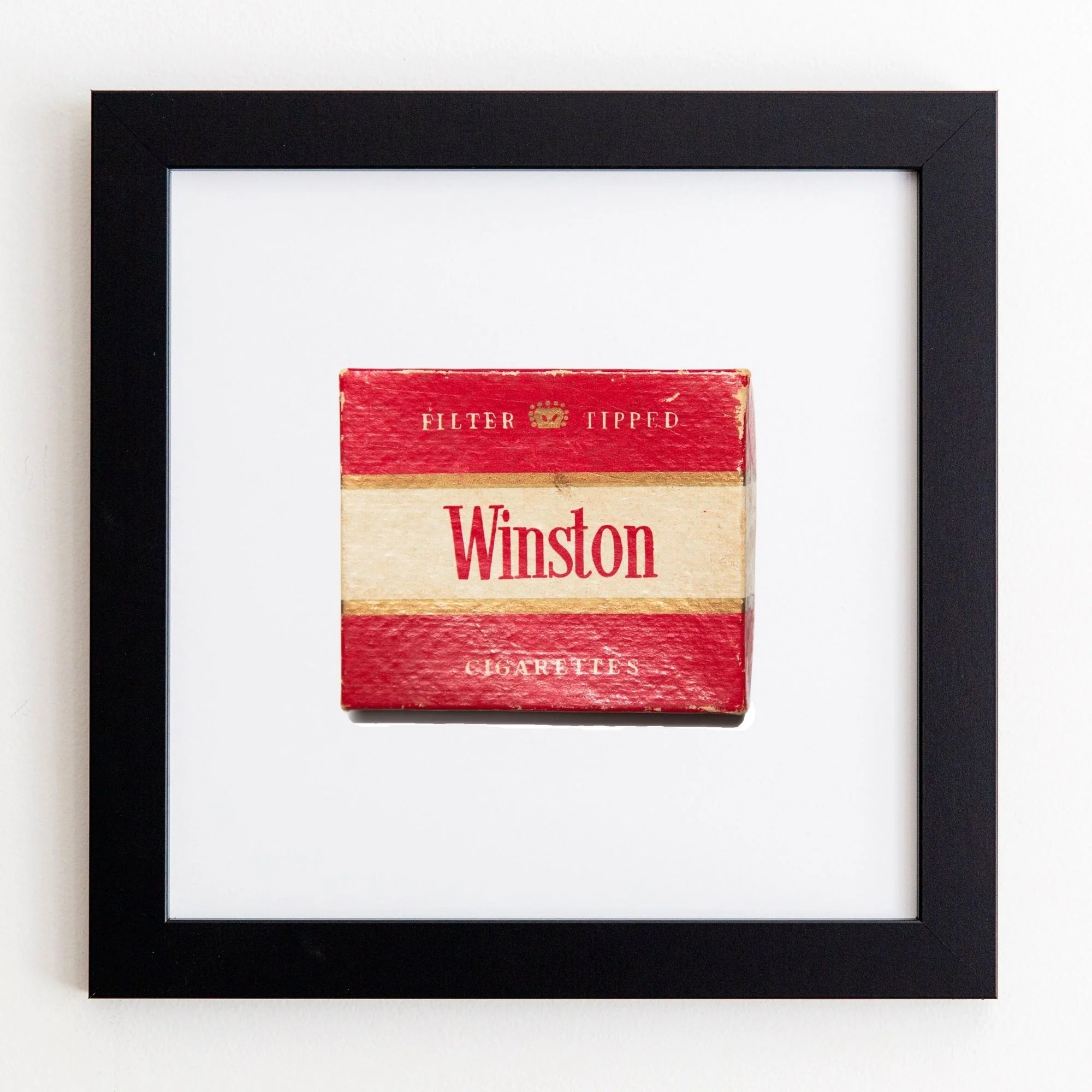 A vintage Winston cigarette pack, prominently red and white, is displayed within a Match South Art Square Black Frame on a white wall. The pack is labeled &quot;Filter Tipped.