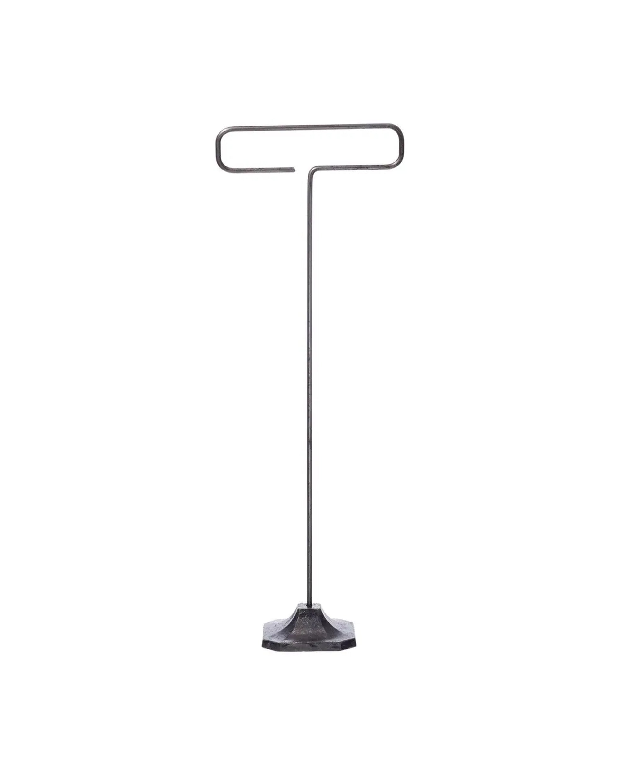 The Desk Wire Display Stand L by Faire features a minimalist design with a flat hexagonal base and a single steel rod that bends into a horizontal loop, creating a T-shape, all crafted from reclaimed steel. Shown against a plain white background.