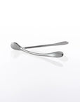 The Wishbone /Small, a pair of sleek, handcrafted aluminum tongs with rounded ends, rests on a glossy white surface, casting a subtle reflection.