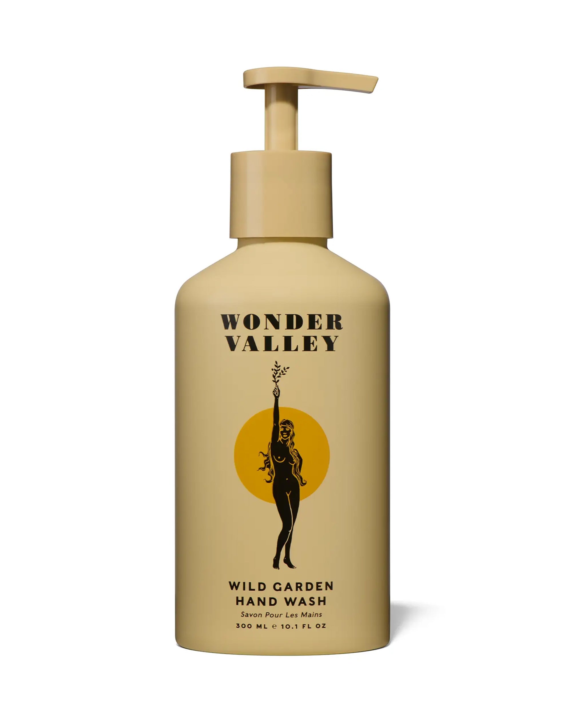 A beige pump bottle labeled "Faire Wild Garden Hand Wash" features a woman with wild herbs before a yellow circle, evoking cedar and botanical notes with its simple, modern design.