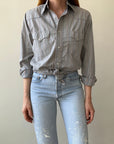 A person wears the 80s Wrangler Button Up from Red Vintage Co., sleeves rolled and tied at the waist, paired with high-waisted light blue jeans with white paint splatters.
